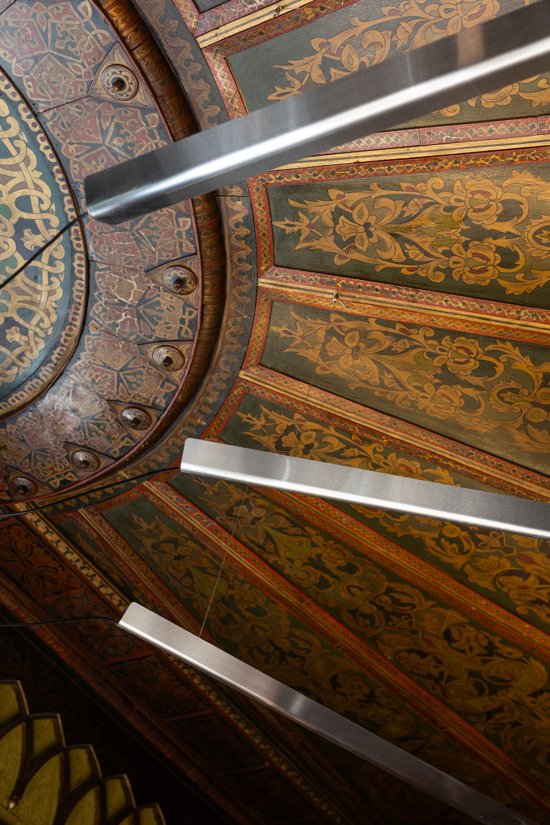 Detail of painted ceiling panels with gilded borders and decorative foliate patterns between timber beams