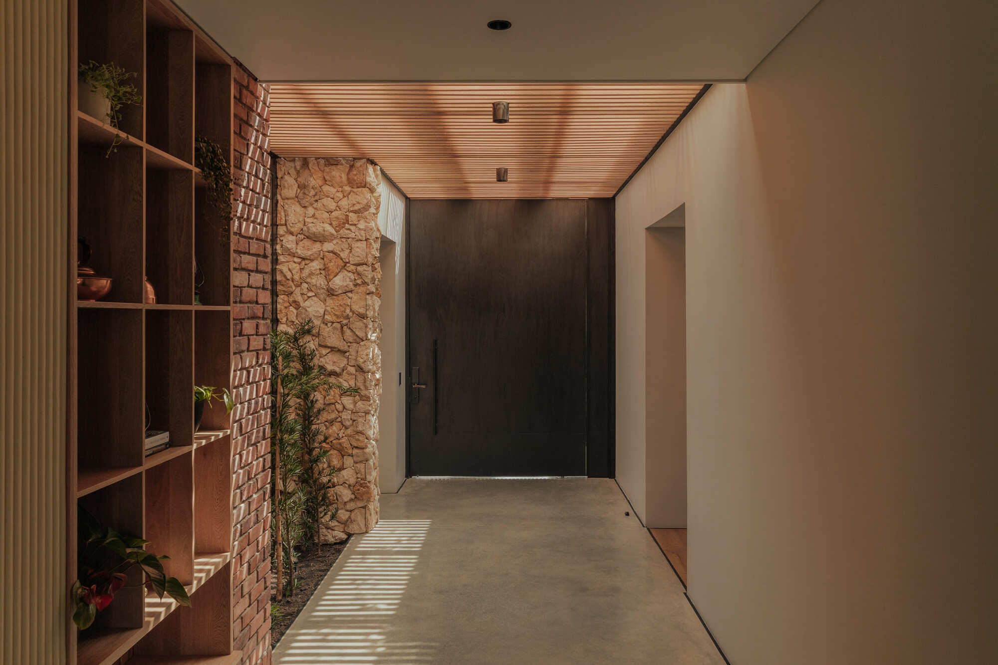 Interior hallway with timber slatted ceiling, brick wall, stone wall and wooden shelving catching afternoon light