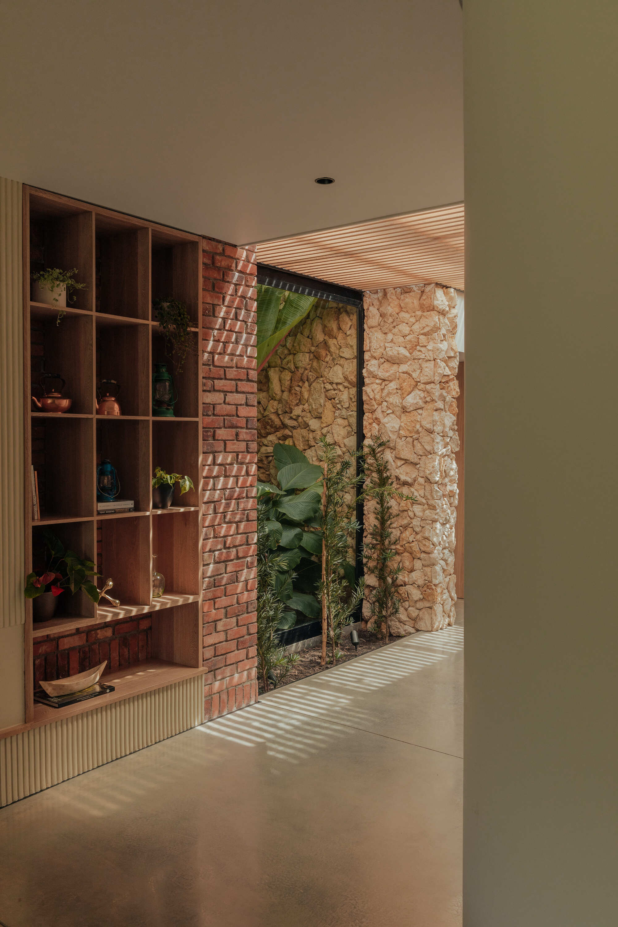 Interior hallway with timber shelving unit, red brick column and limestone wall framing courtyard view
