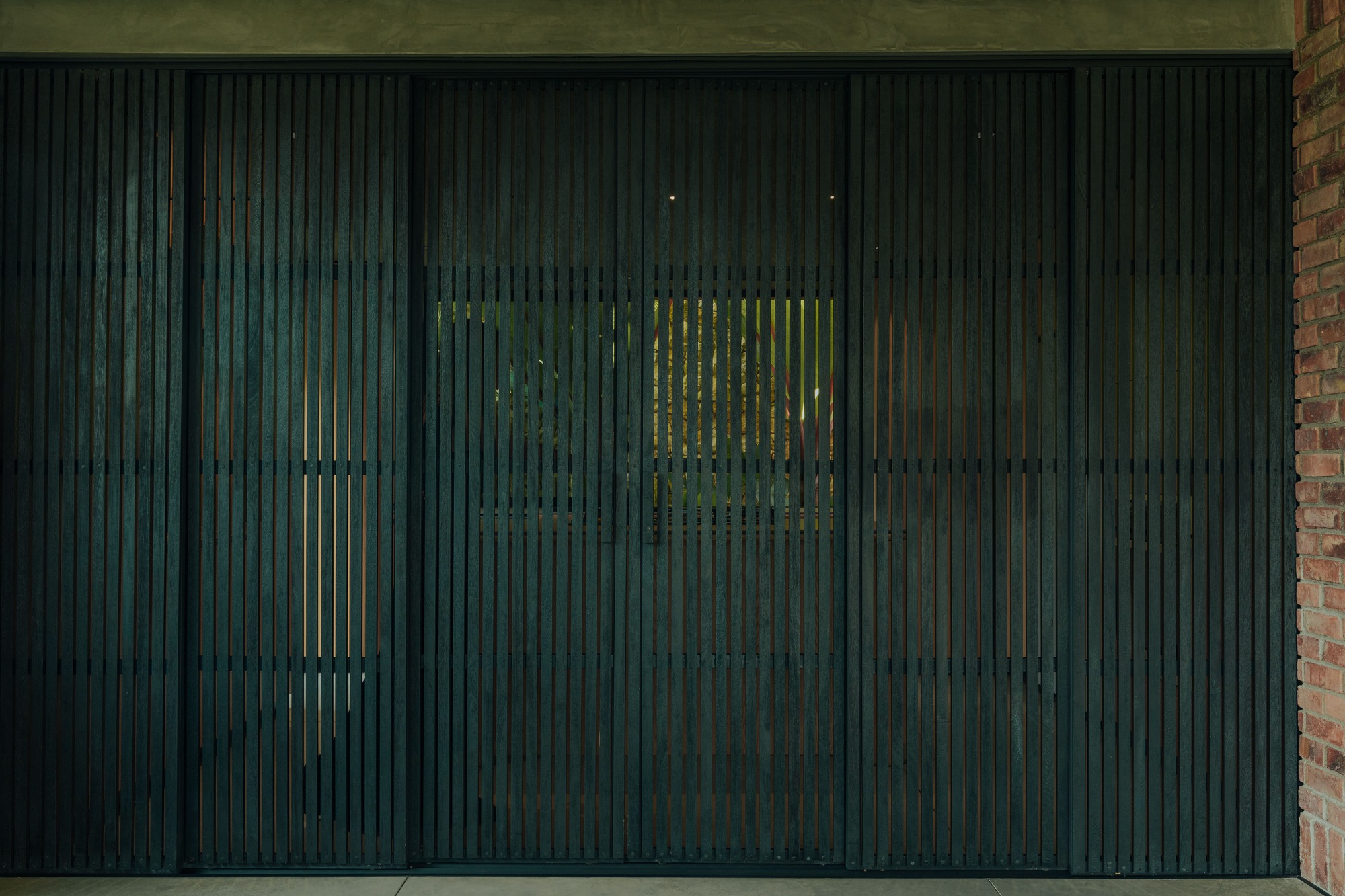 Dark timber vertical slat screen with glimpses of greenery visible through the gaps