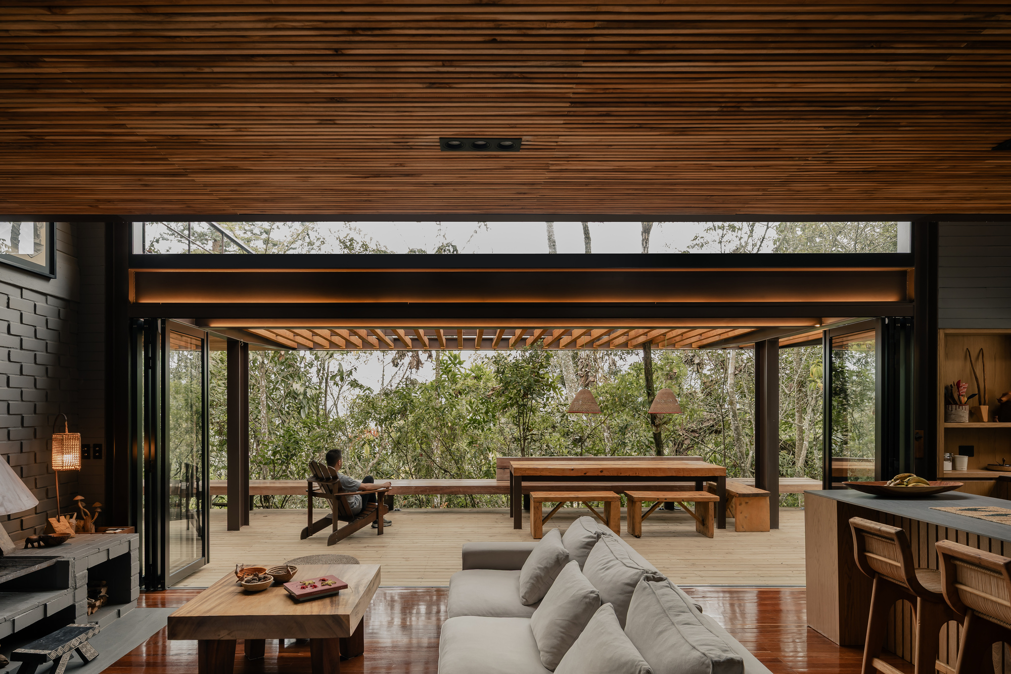 Living space opening to covered deck with timber pergola and figure seated in forest clearing