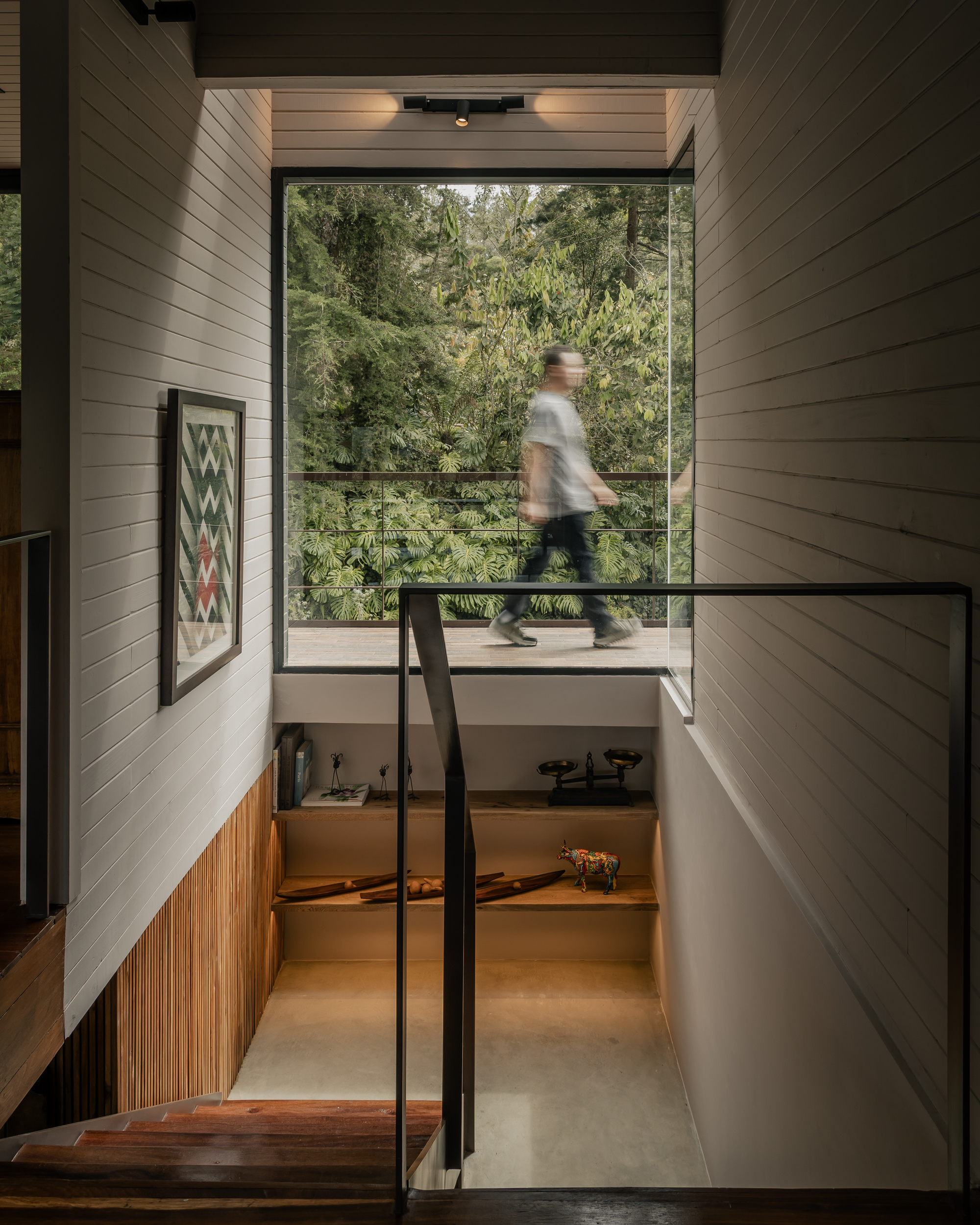 Split-level stairwell with blurred figure crossing glass bridge above painted wood walls