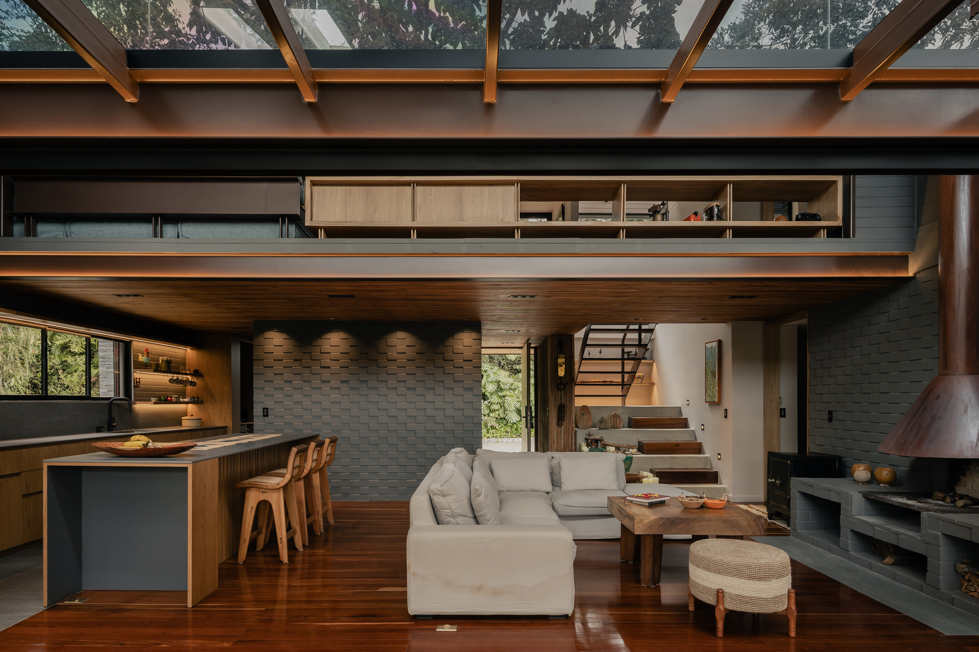 Double-height living area with timber mezzanine, textured concrete block wall, and clerestory windows filtering daylight