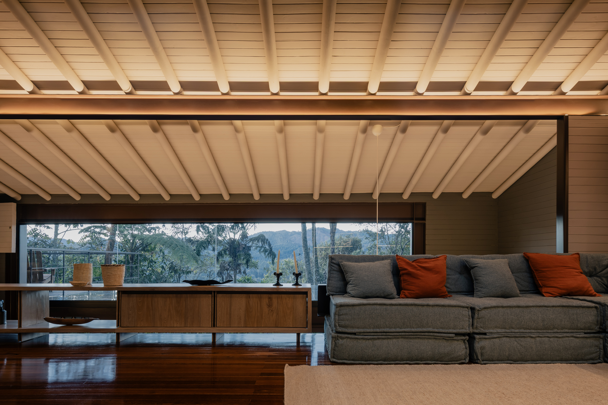 Living room with exposed timber beam ceiling and horizontal windows framing forest views
