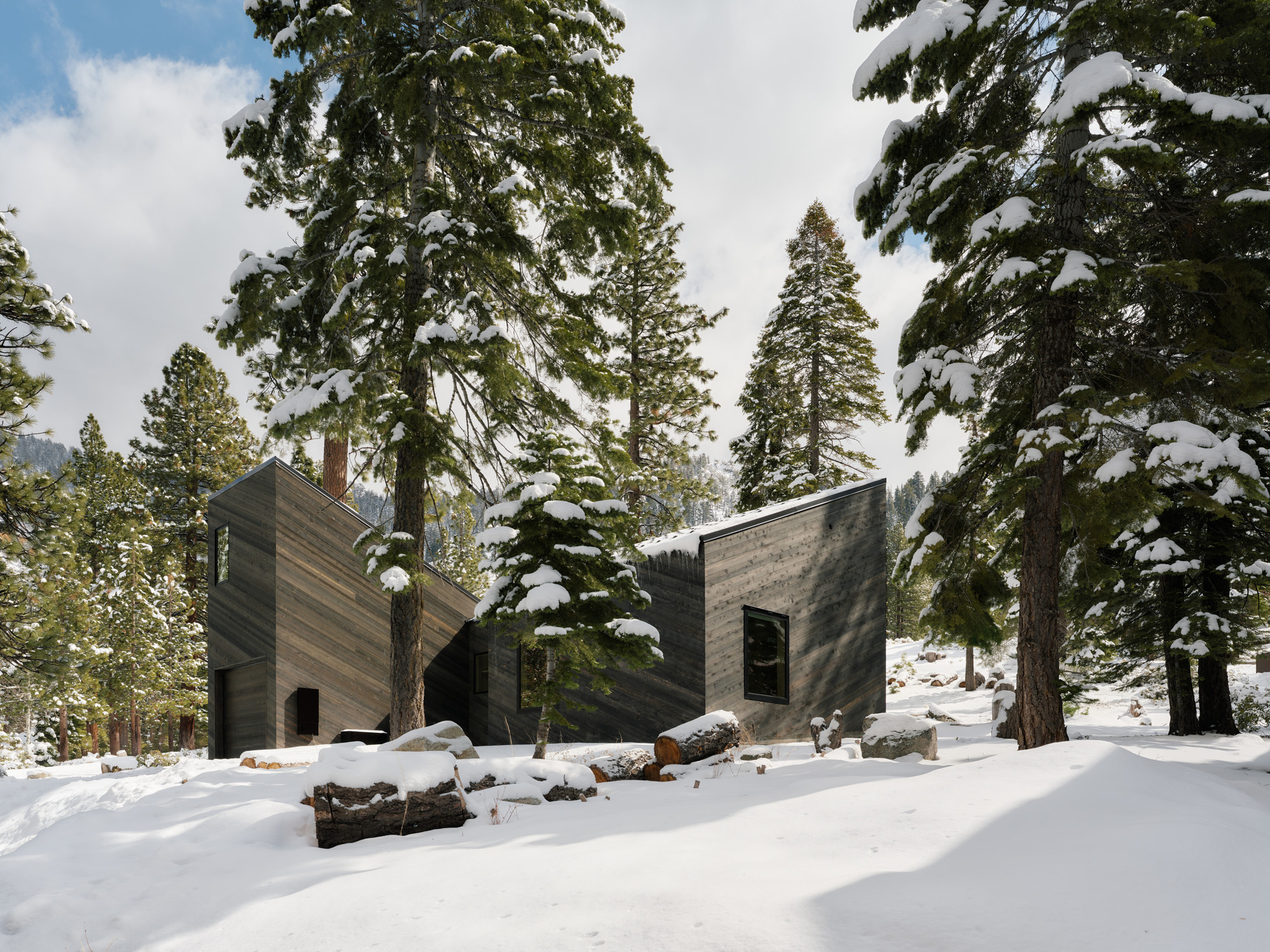Facade of interlocking wood clad volumes framed by snow covered conifers and boulders