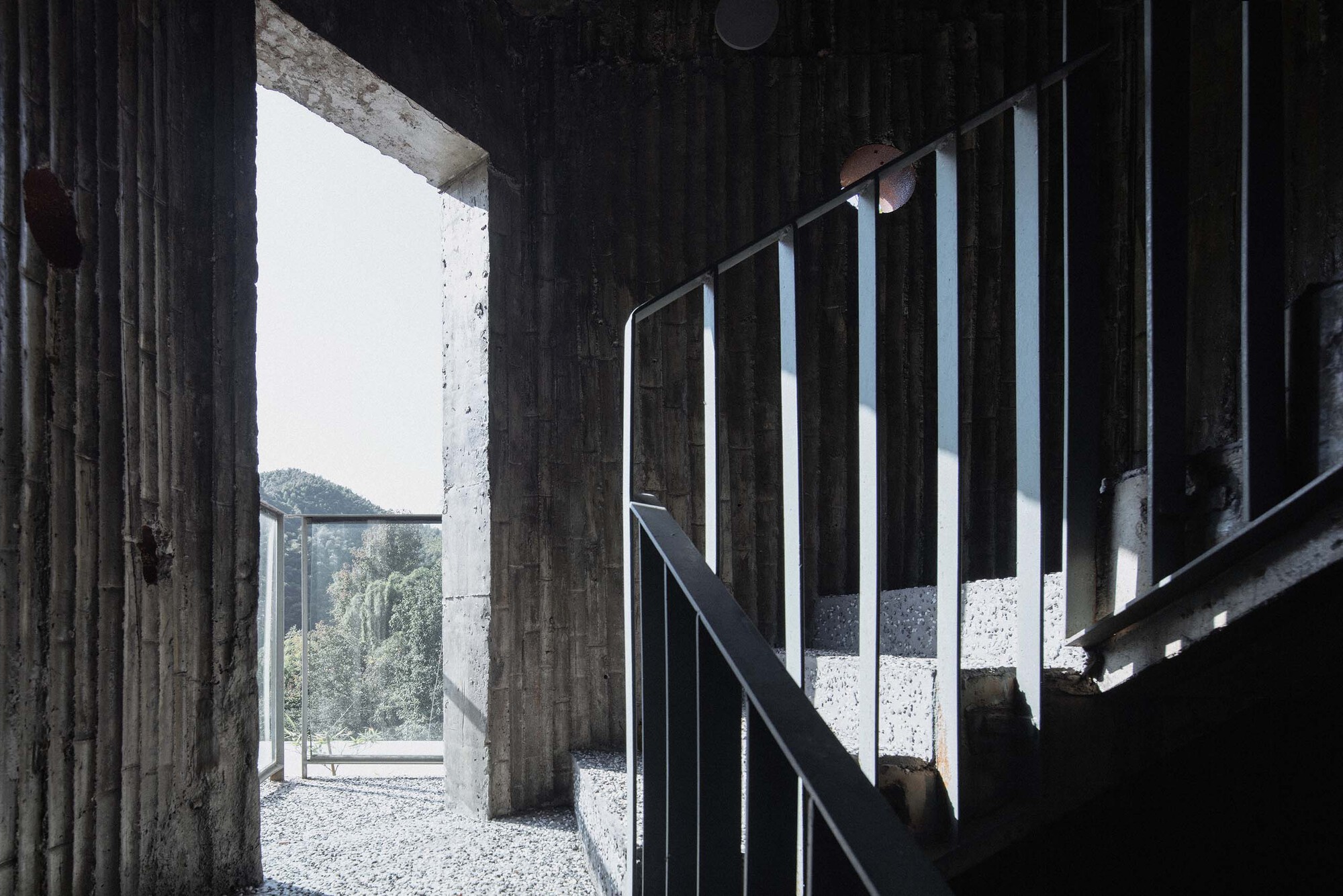 Interior staircase with steel railings framed by board-formed concrete walls and gravel floor