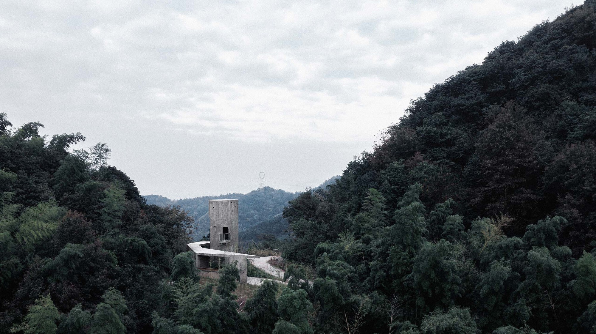 Concrete tower and low-lying roof nestled in a forested valley beneath overcast skies