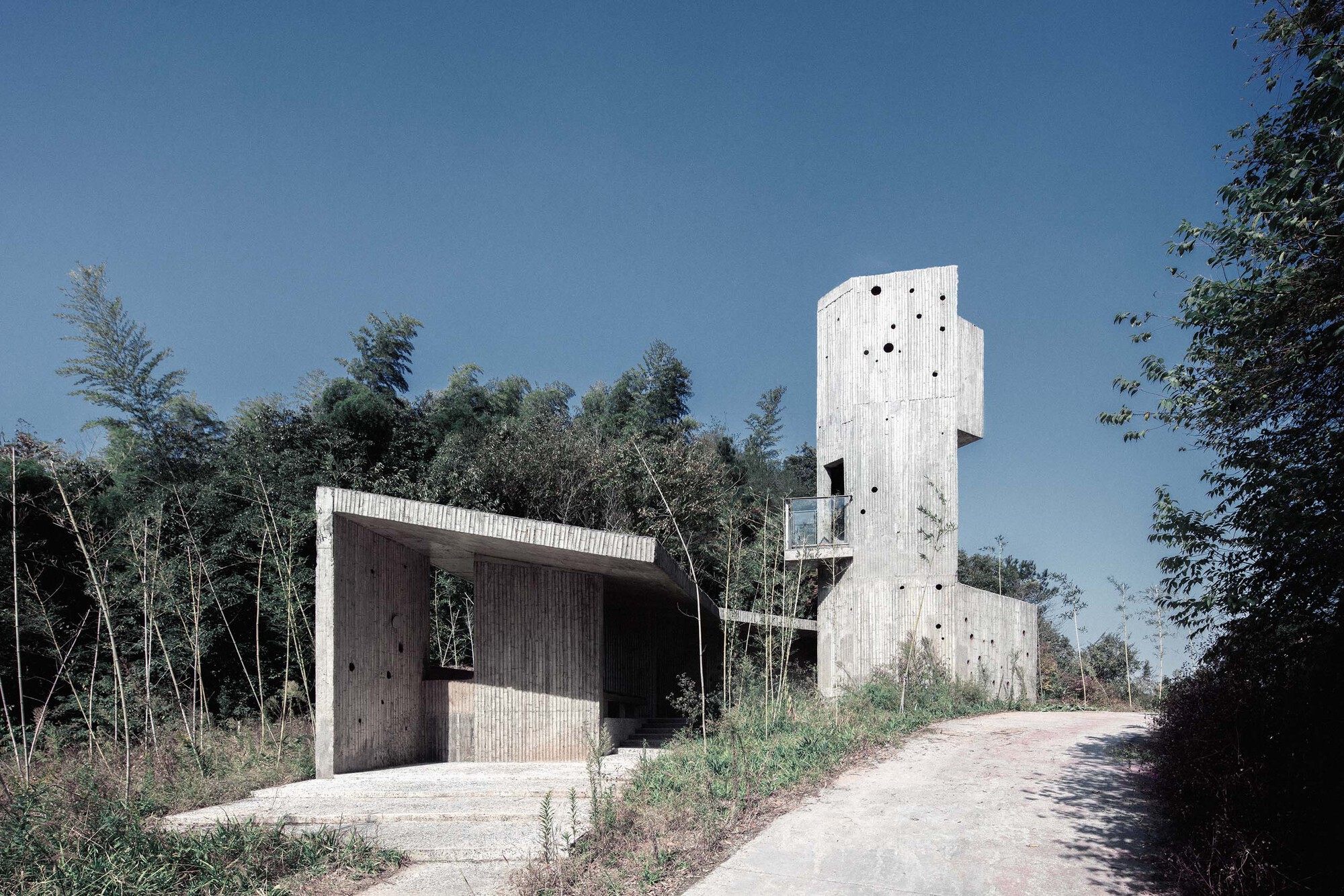 Entrance pavilion with ribbed concrete walls and tower structure under clear blue sky