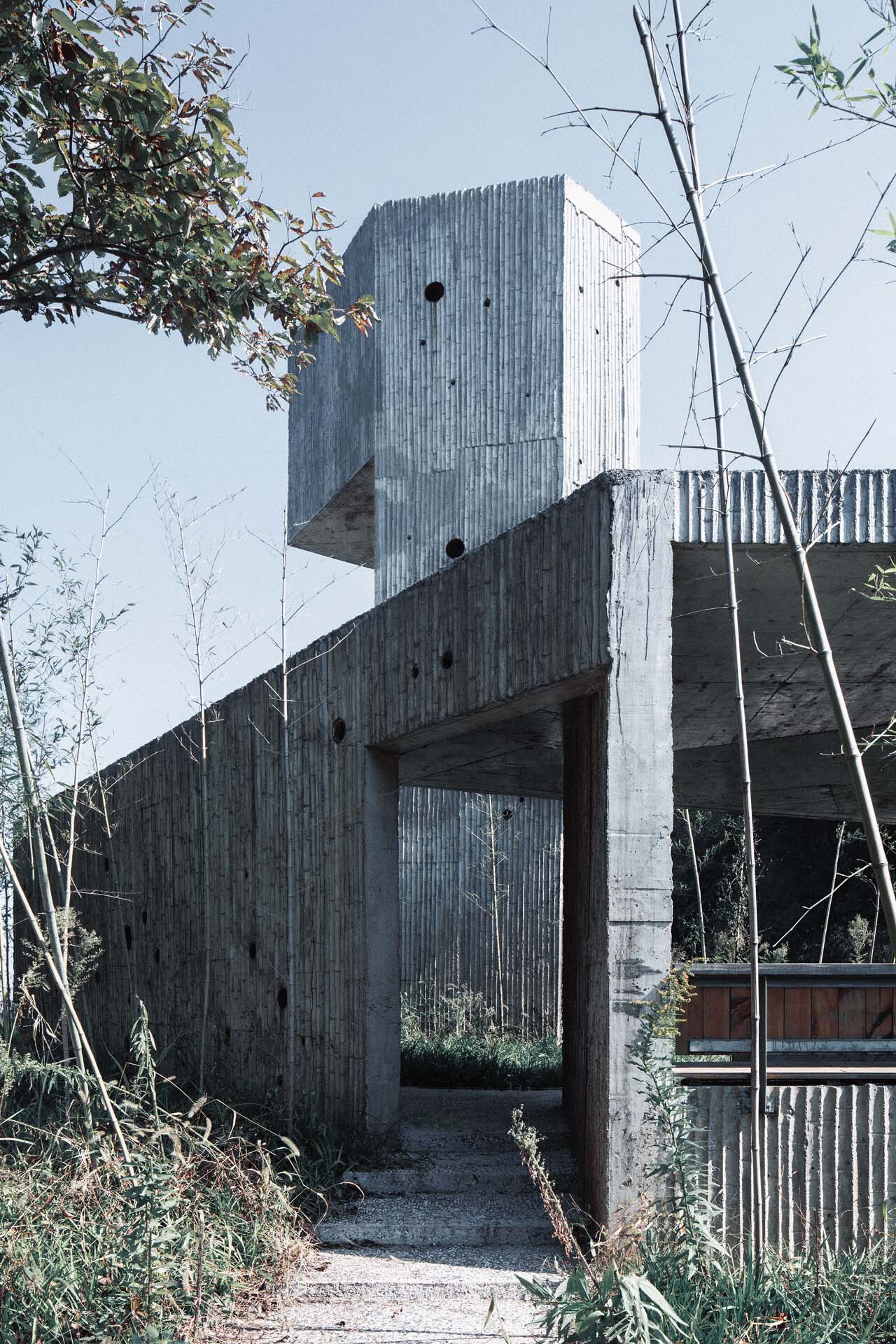 Covered entry passage beneath cantilevered concrete volumes with board-formed surfaces and circular openings