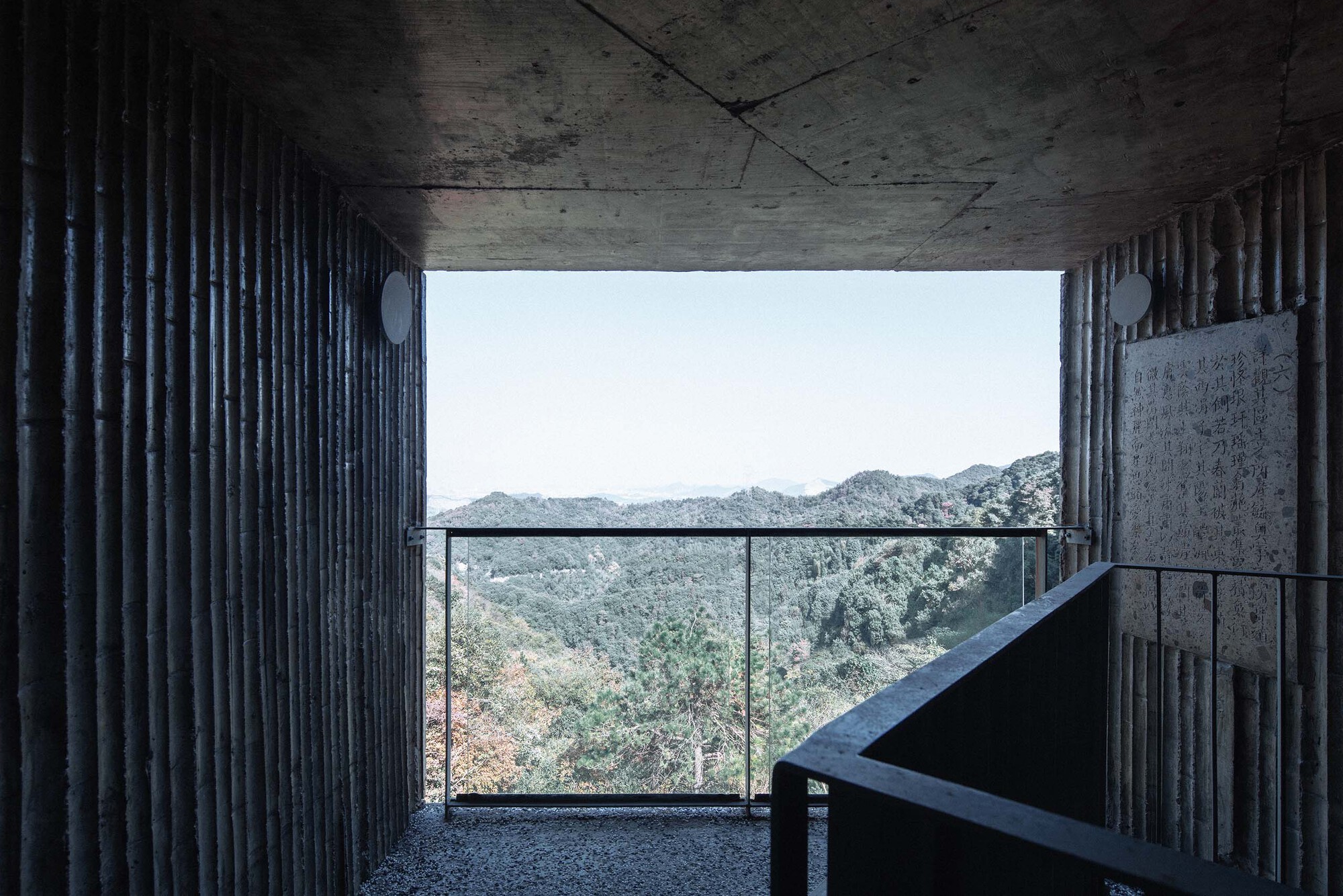 Concrete balcony with glass railing opening to distant mountain ridges under overcast sky