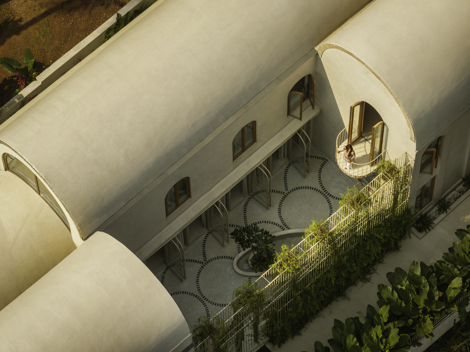 Aerial view of vaulted roof forms sheltering courtyard with circular pavers and planted balconies in afternoon light