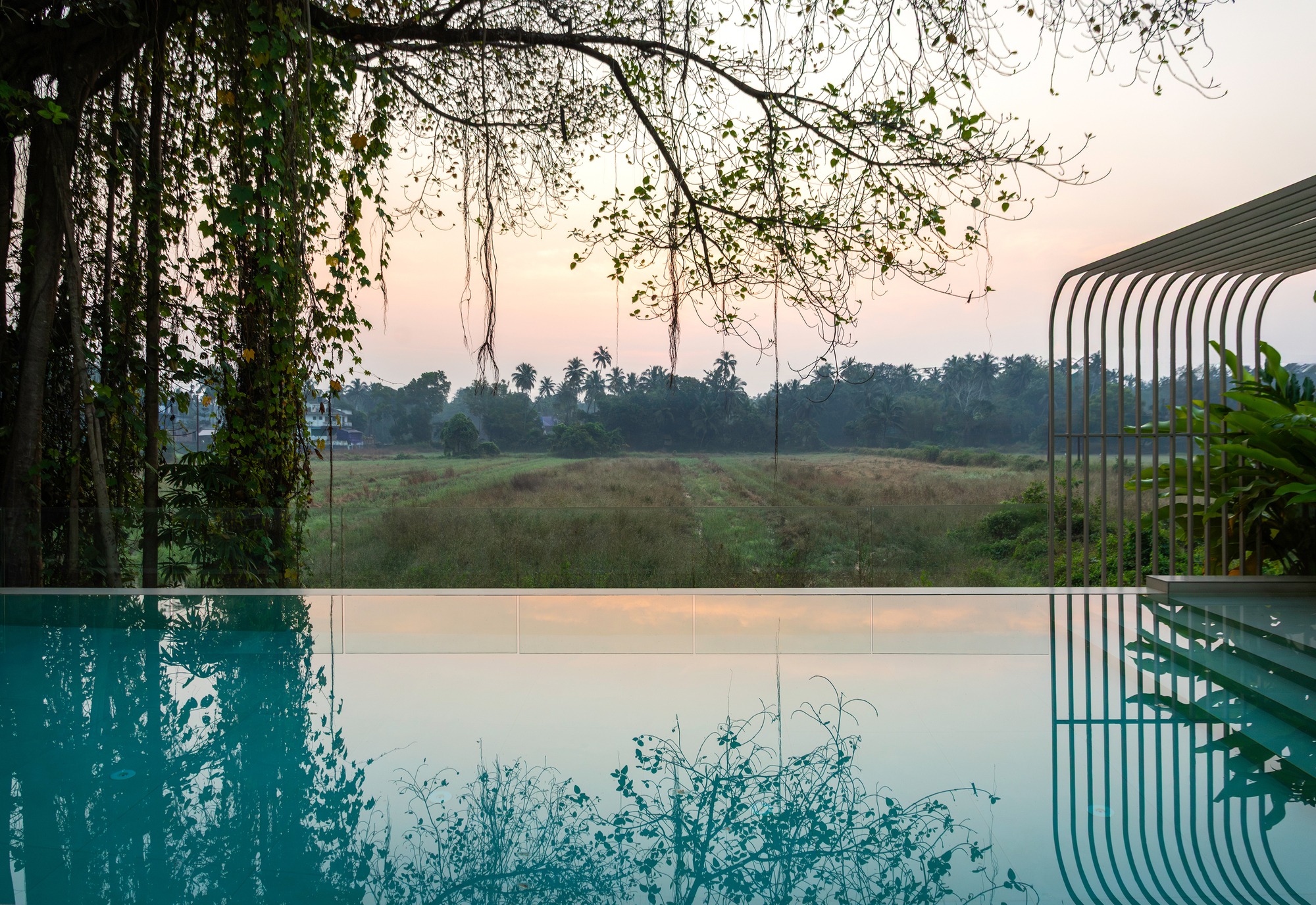Infinity pool edge with curved metal canopy overlooking fields at dusk