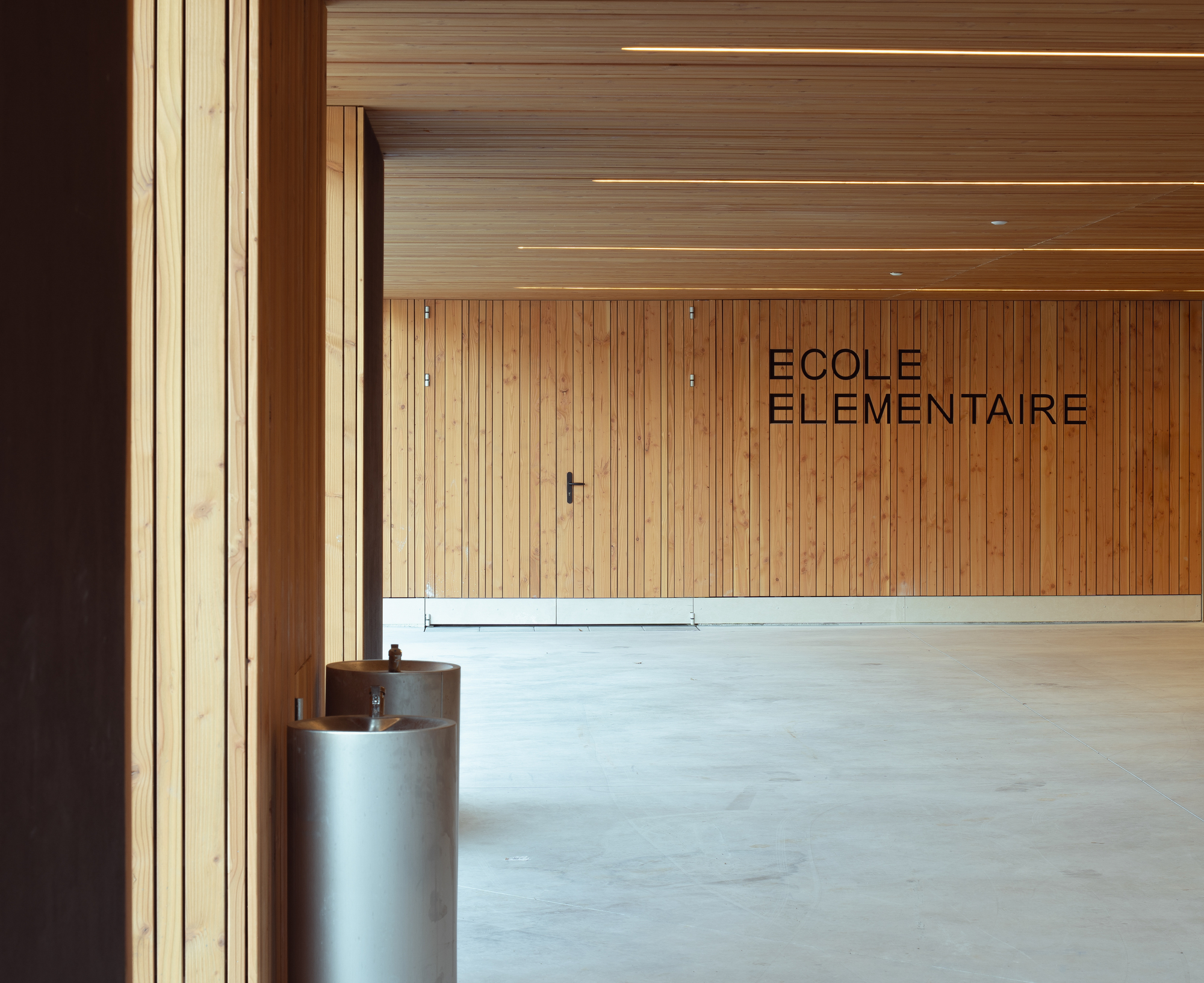 Timber-lined entrance hall with cylindrical water fountain beside vertical slat cladding