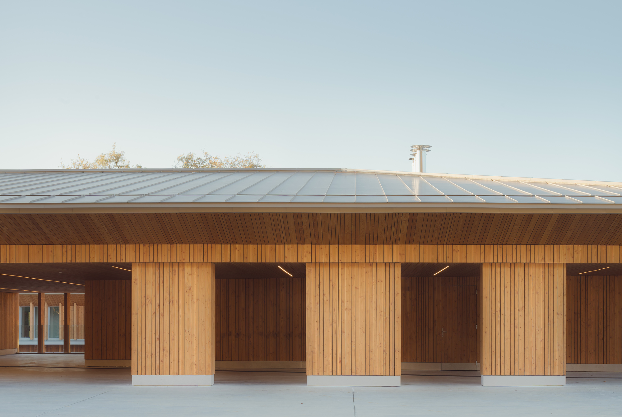 Covered walkway with vertical timber cladding and recessed bays beneath a standing seam metal roof