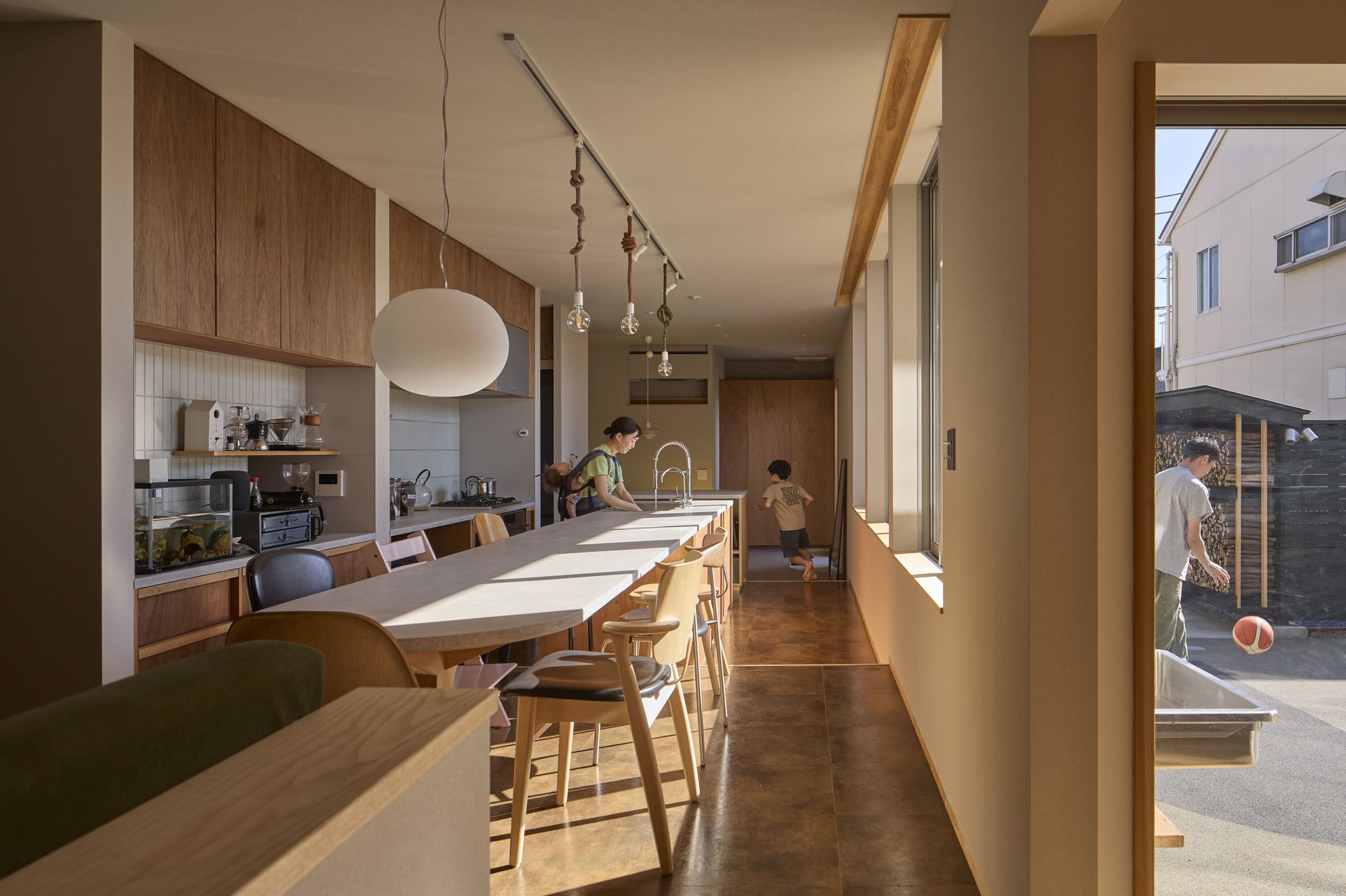 Kitchen and dining area with timber cabinetry and a long table flooded with afternoon sunlight