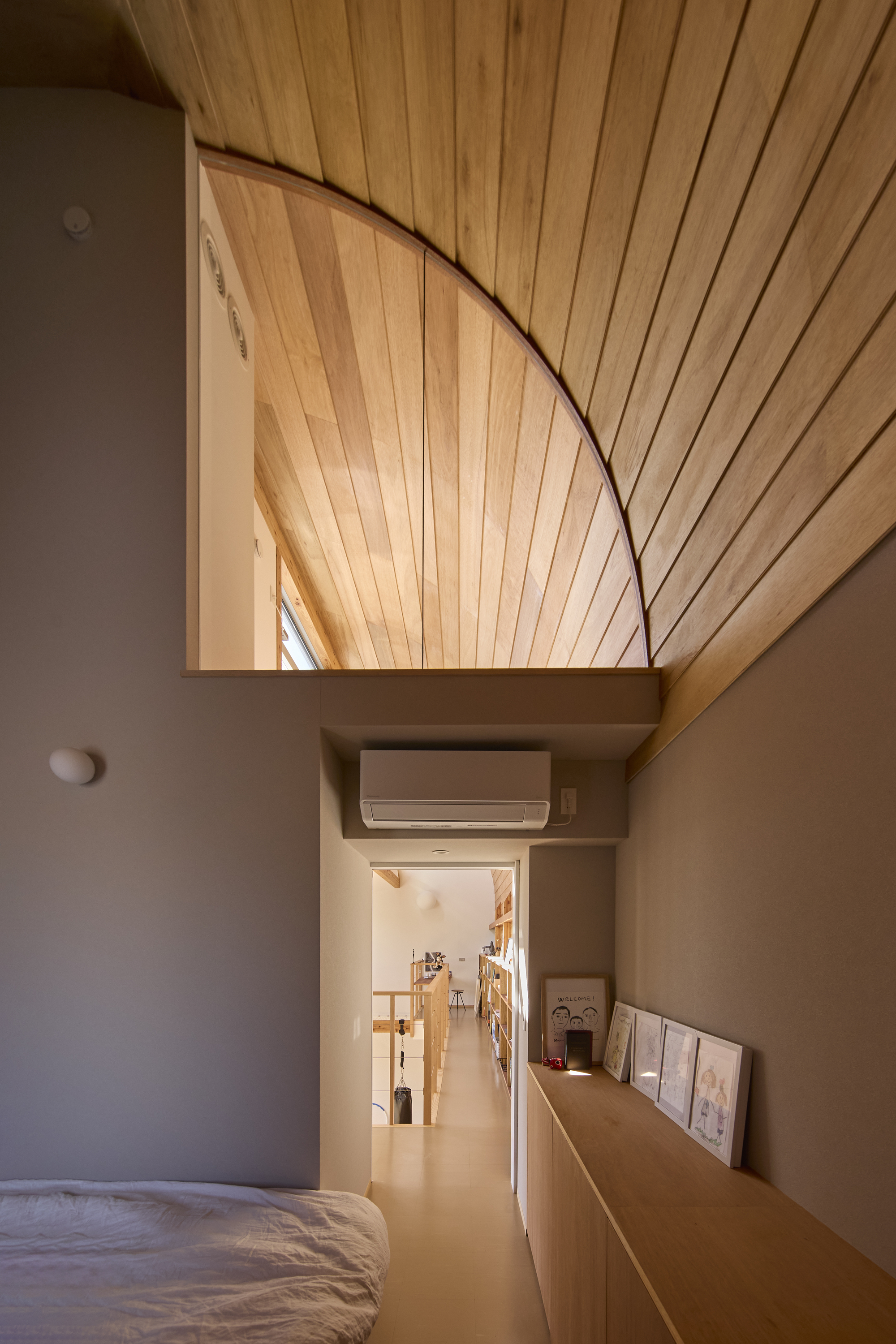 Bedroom view through a grey-framed opening showing the curved timber ceiling vault above a corridor