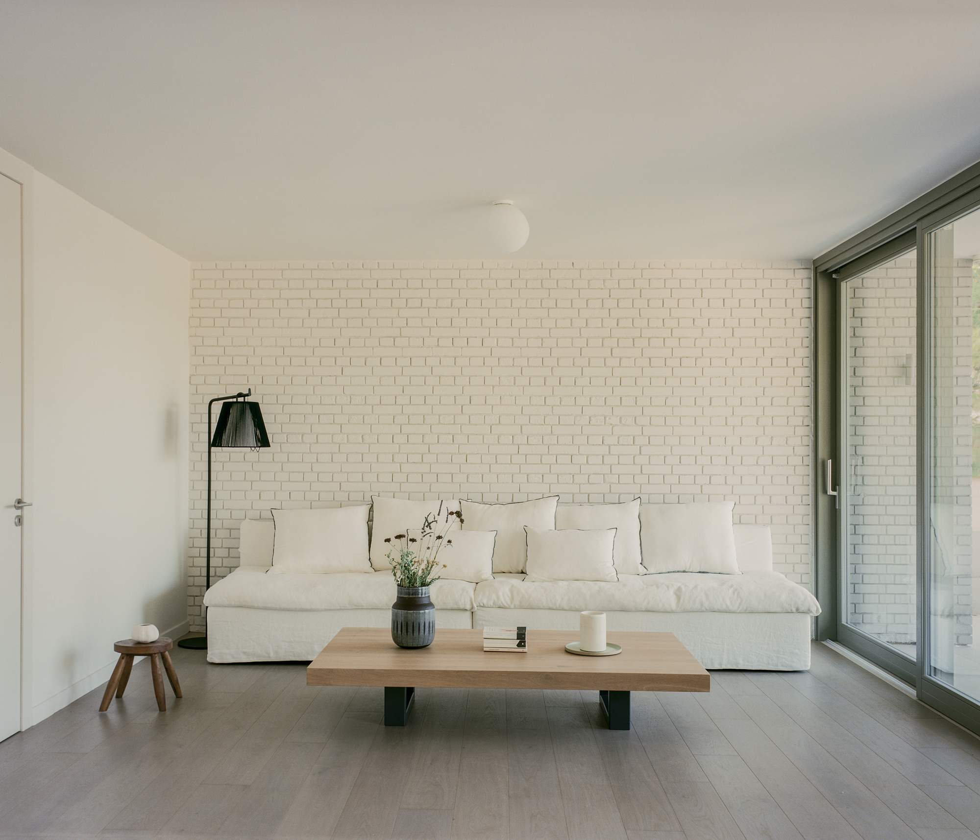 Living room with white brick wall, wood coffee table, and floor-to-ceiling sliding glass doors