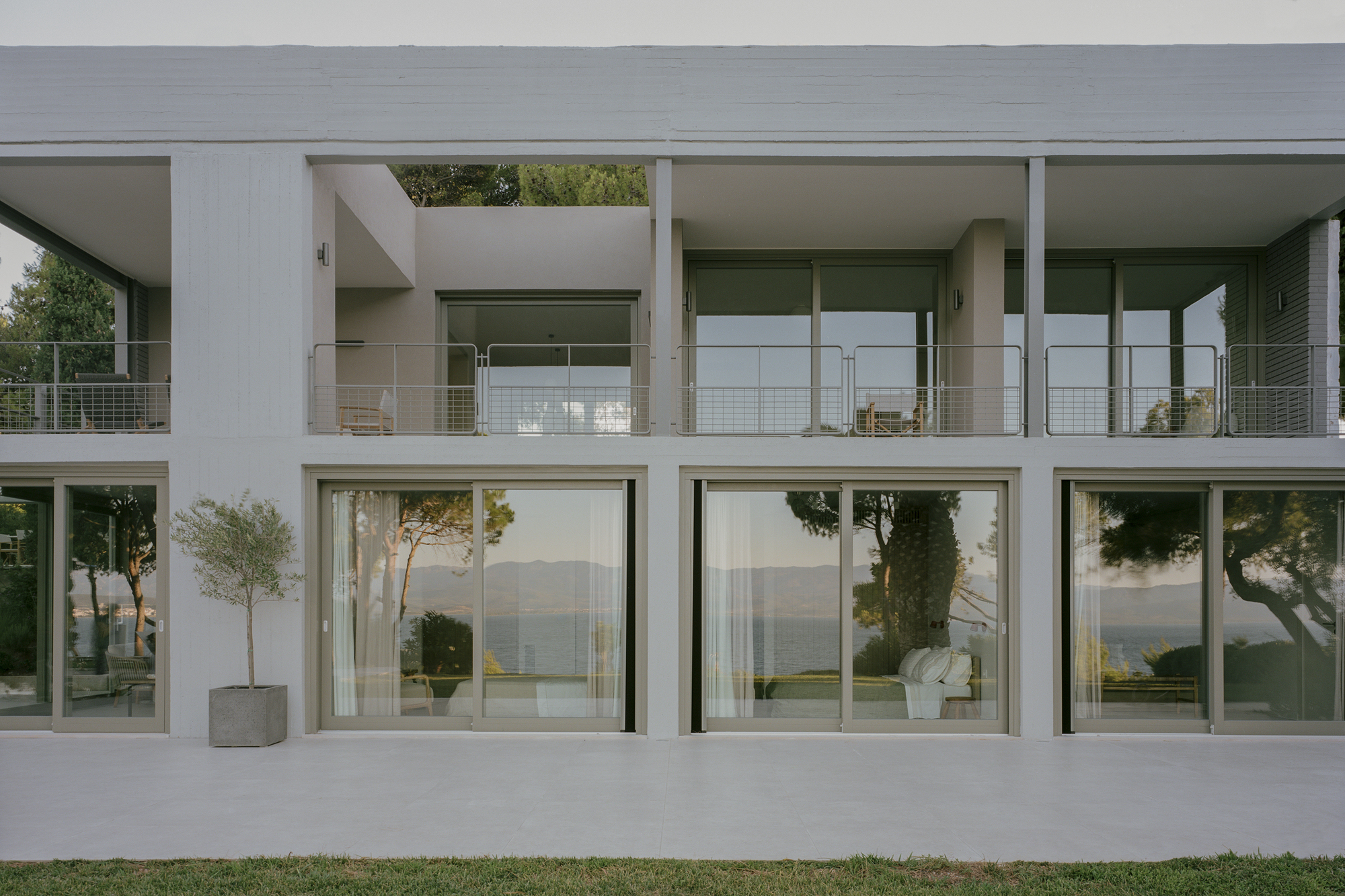 Courtyard terrace with floor-to-ceiling glazing and potted trees overlooking distant hills at dusk