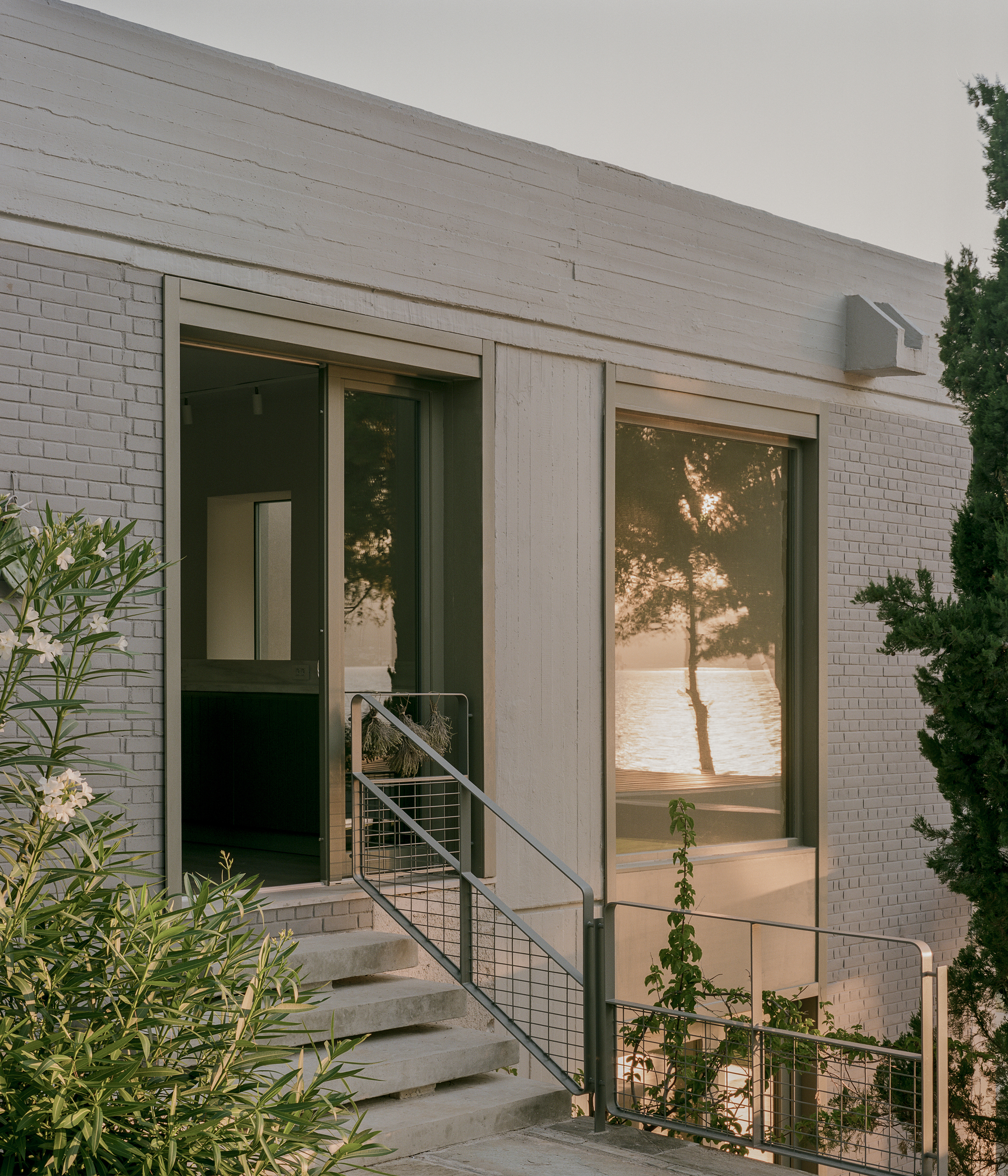Entry with wire mesh balustrade and concrete steps against white brick wall at sunset