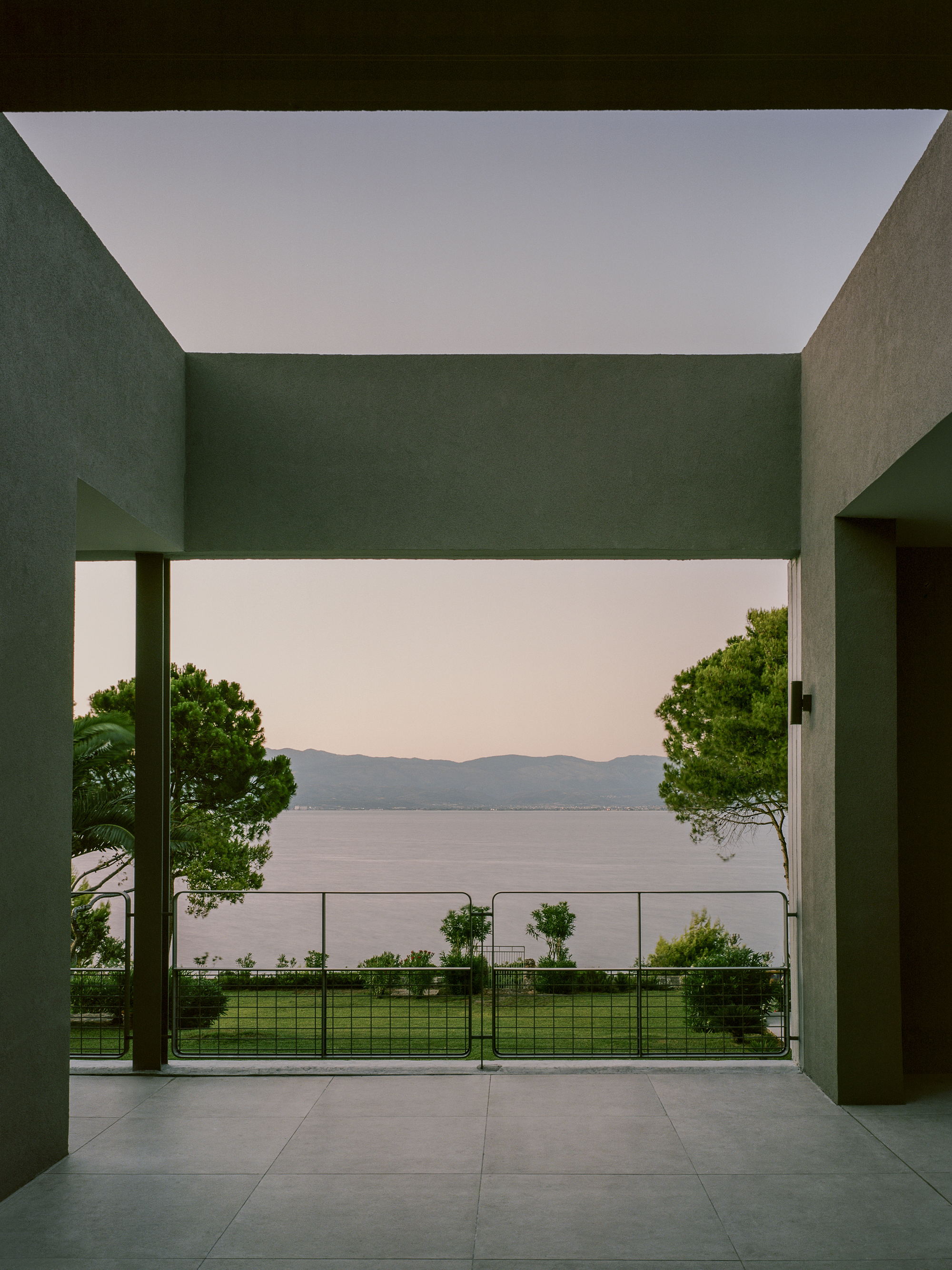 Covered terrace with painted columns framing a view of lawn, trees and distant lake at dusk