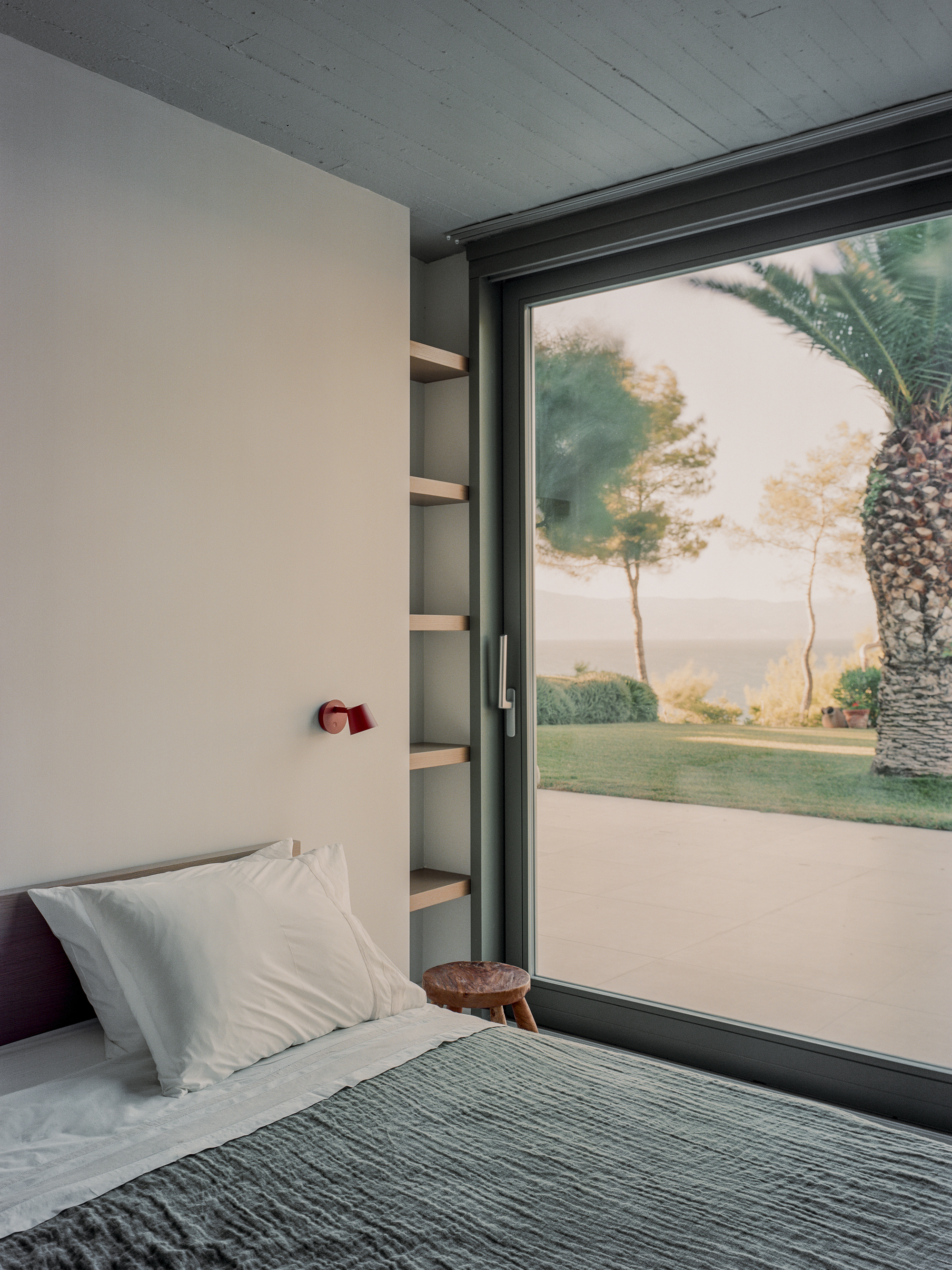 Bedroom with sliding glass door opening to a lawn with palm and pine trees