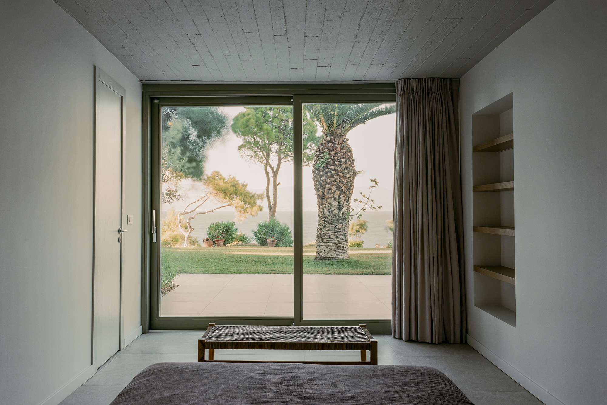 Bedroom with full-height glazed door opening to a courtyard with palm tree and lawn