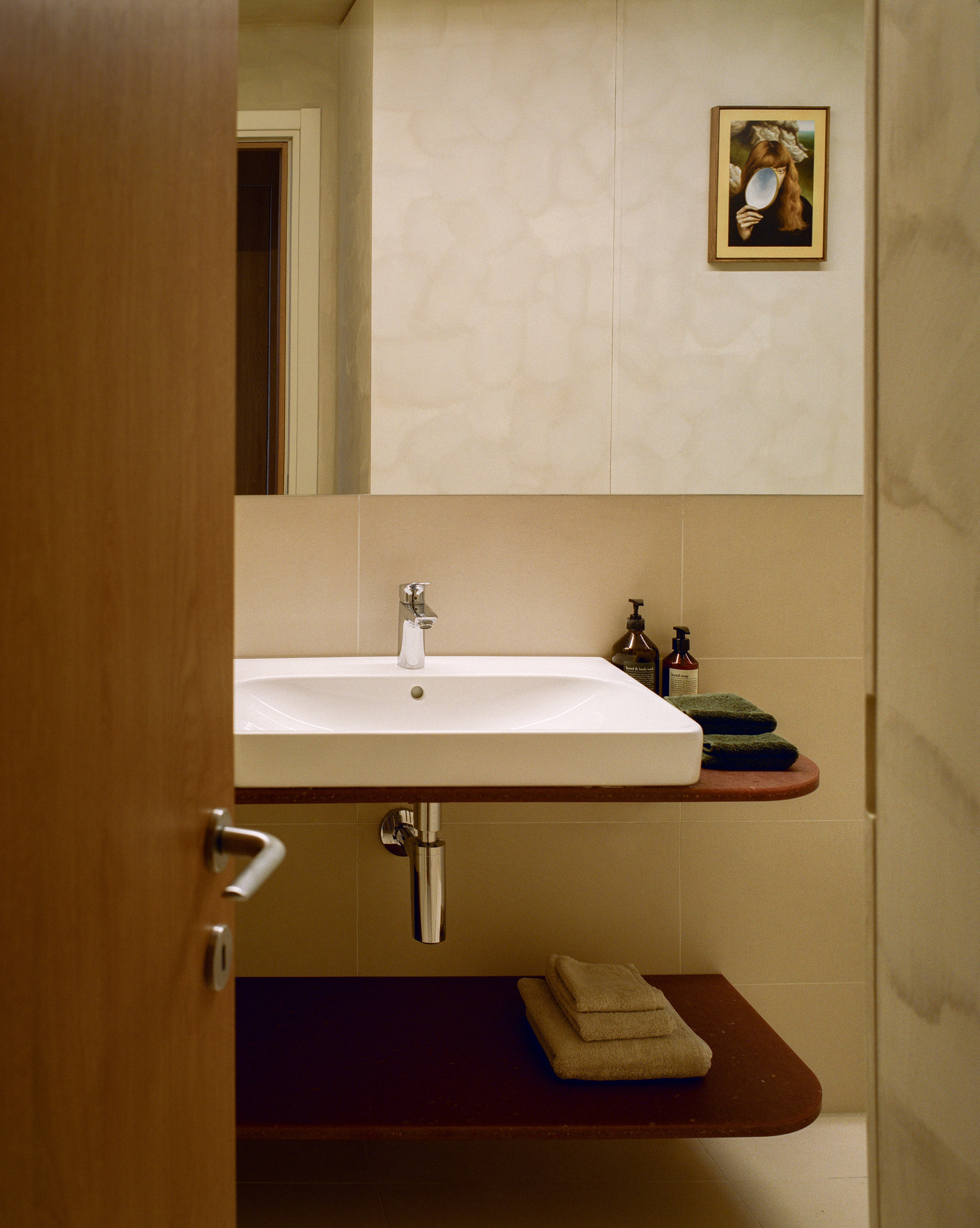 Bathroom vanity with wall-mounted sink and curved timber shelves under reflected doorway