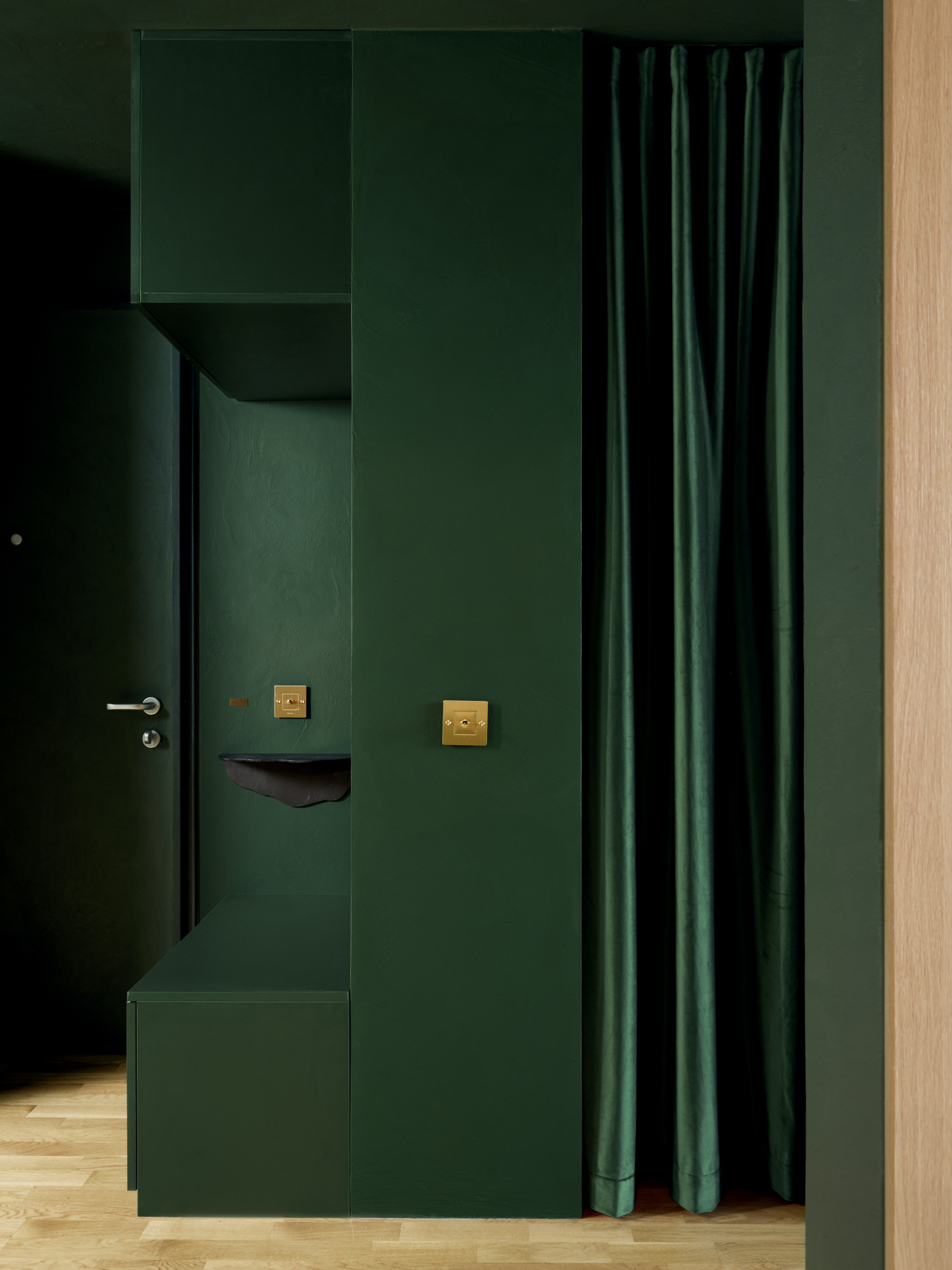Green entryway volume with wall-mounted coat hooks, brass switches, and curtain beside an oak door frame
