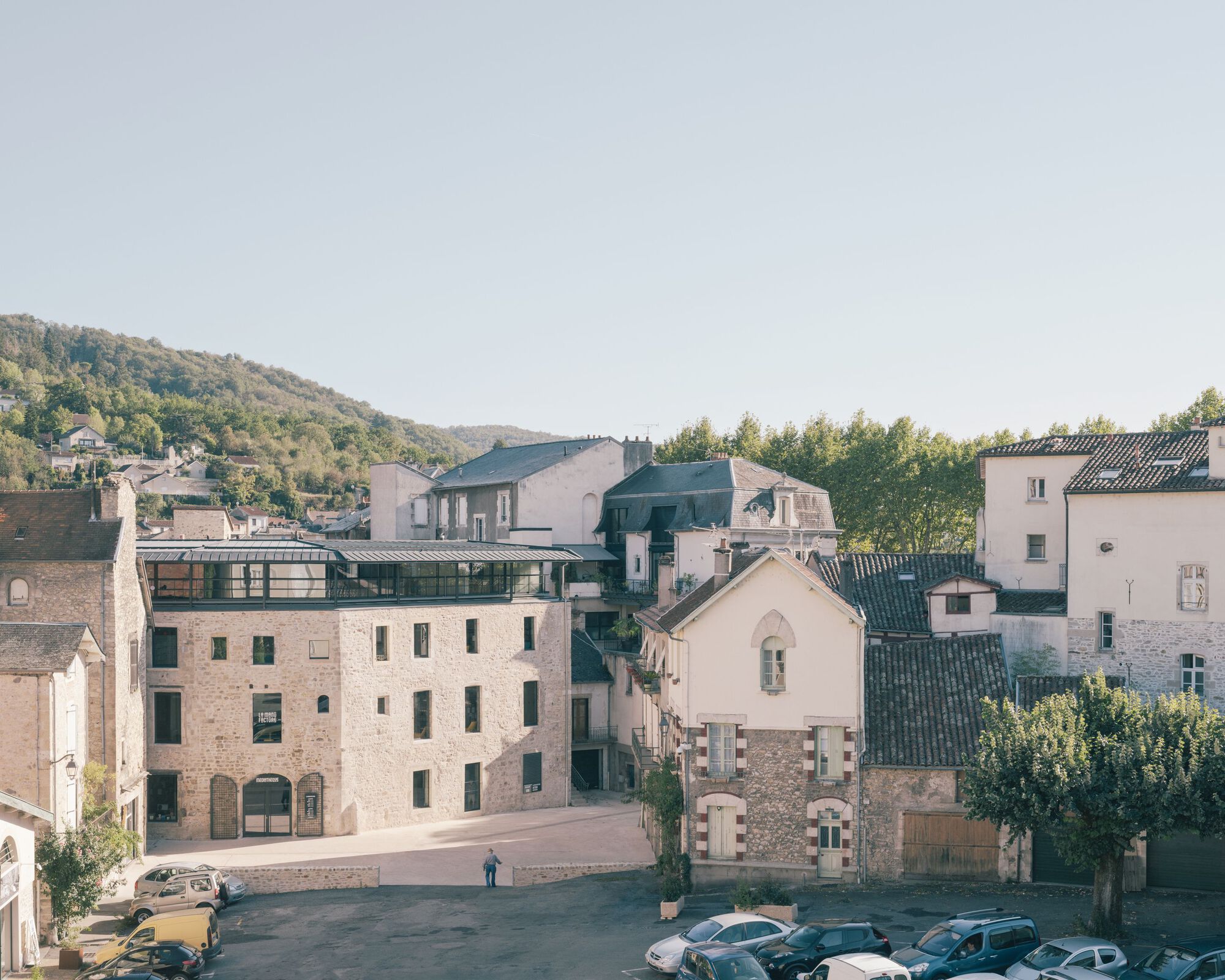Elevated view of clustered stone buildings with a glazed rooftop addition and hillside beyond