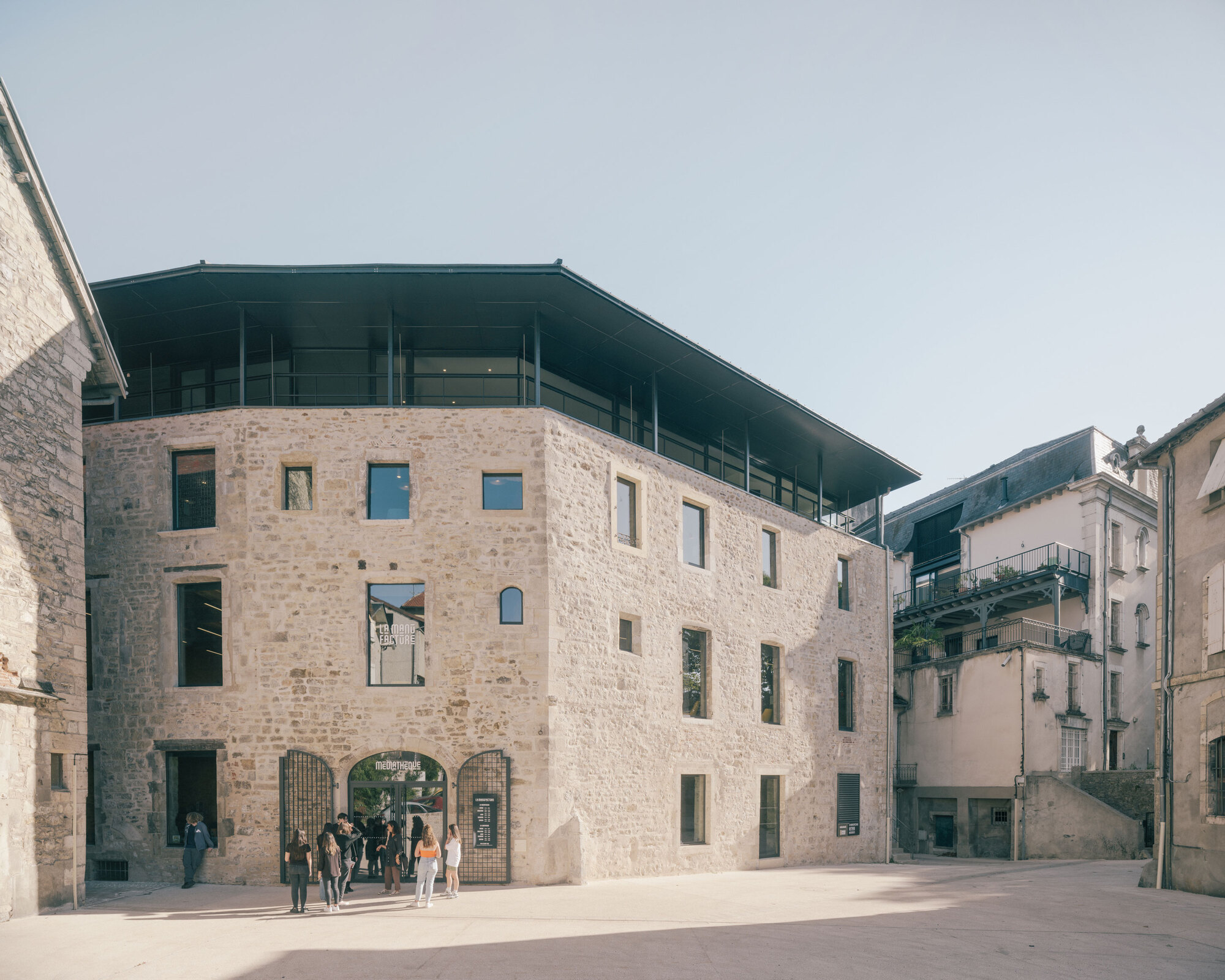 Stone facade with irregular window openings and visitors gathered at the arched ground floor entrance