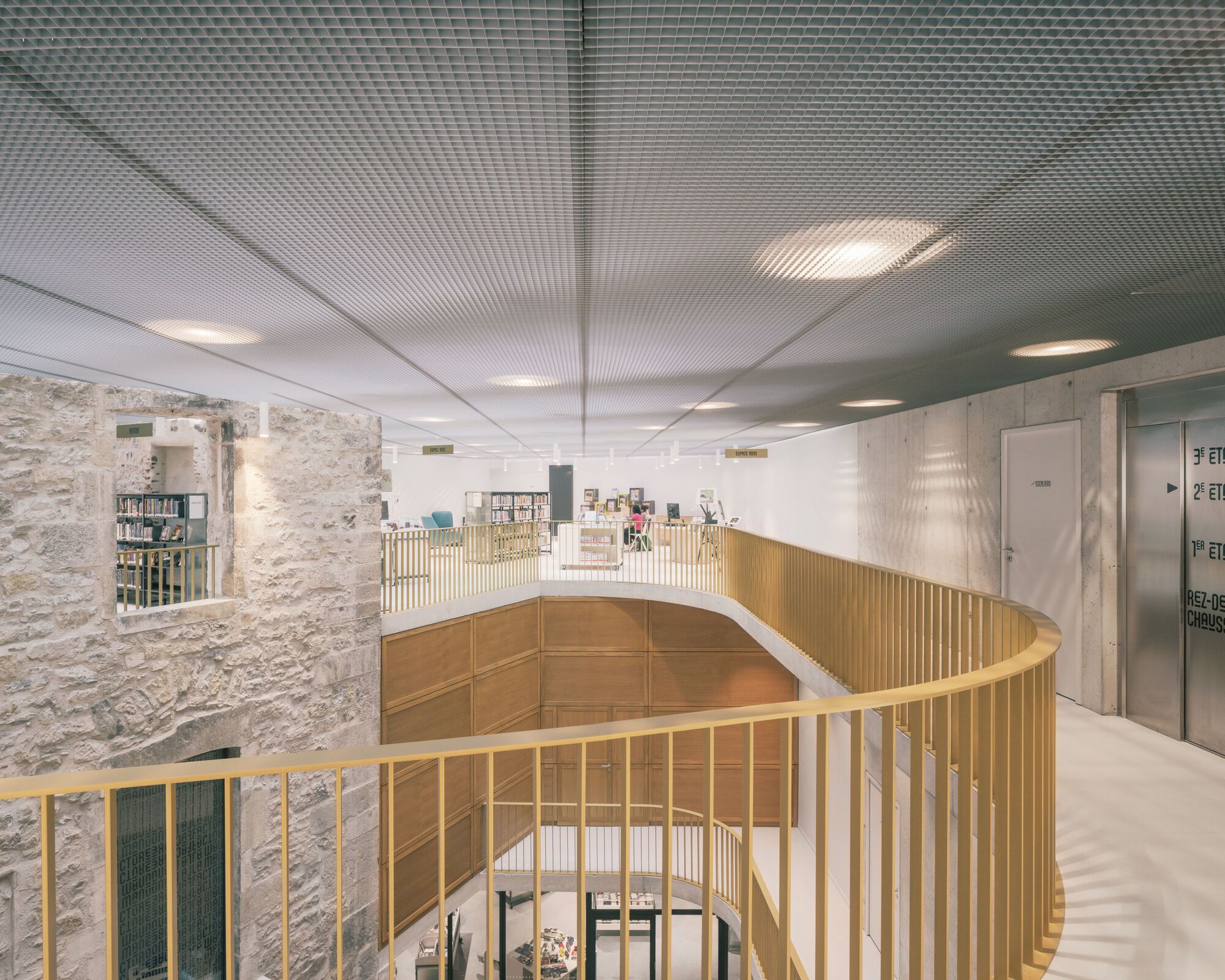 Curved timber balustrade wrapping the atrium void beneath a suspended perforated white metal ceiling