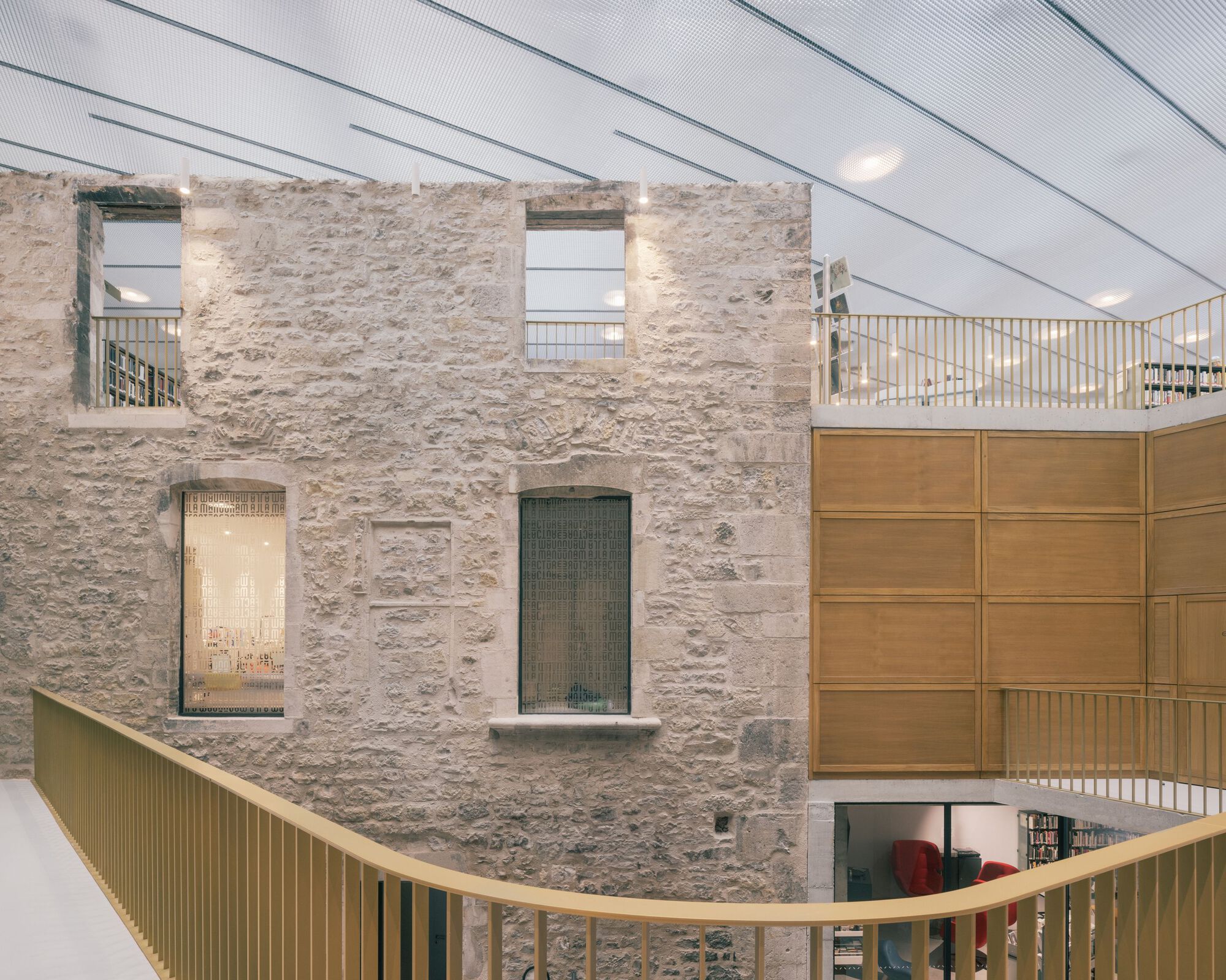 Interior courtyard with retained stone wall and new timber-paneled volumes beneath a translucent roof