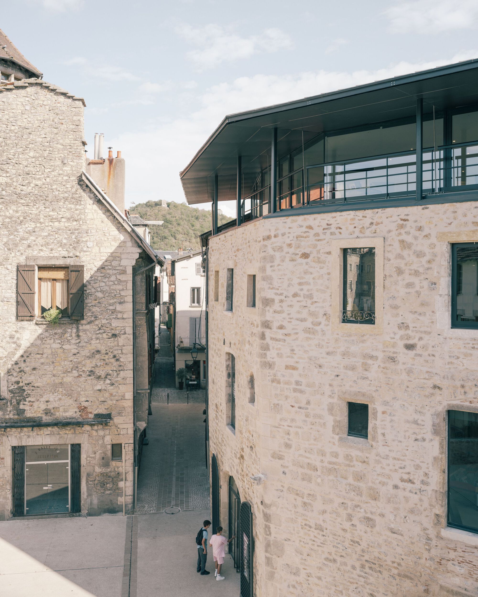 Courtyard view showing stone masonry walls with new steel and glass canopy above two visitors