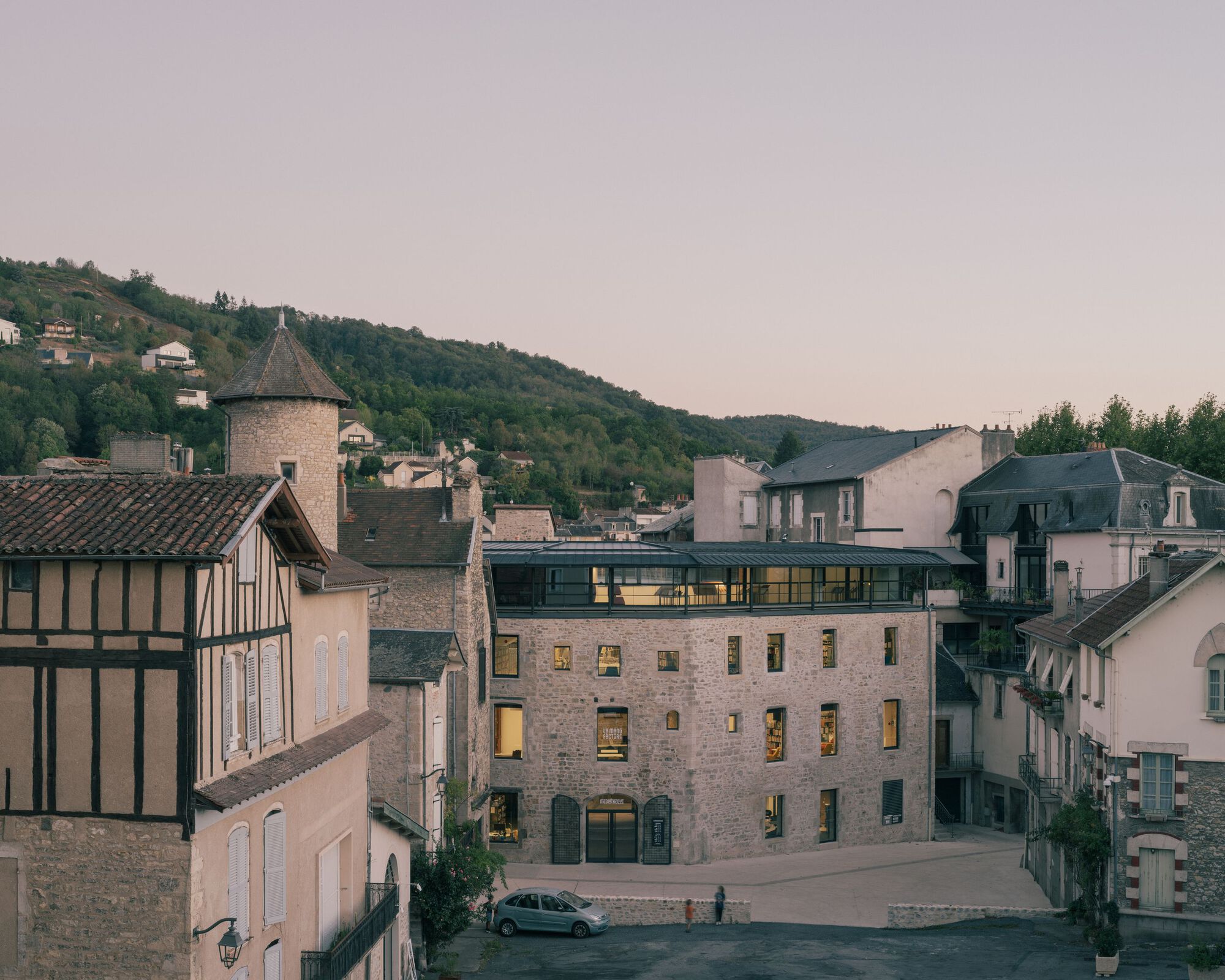 Stone building with illuminated windows nestled among historic village structures at dusk