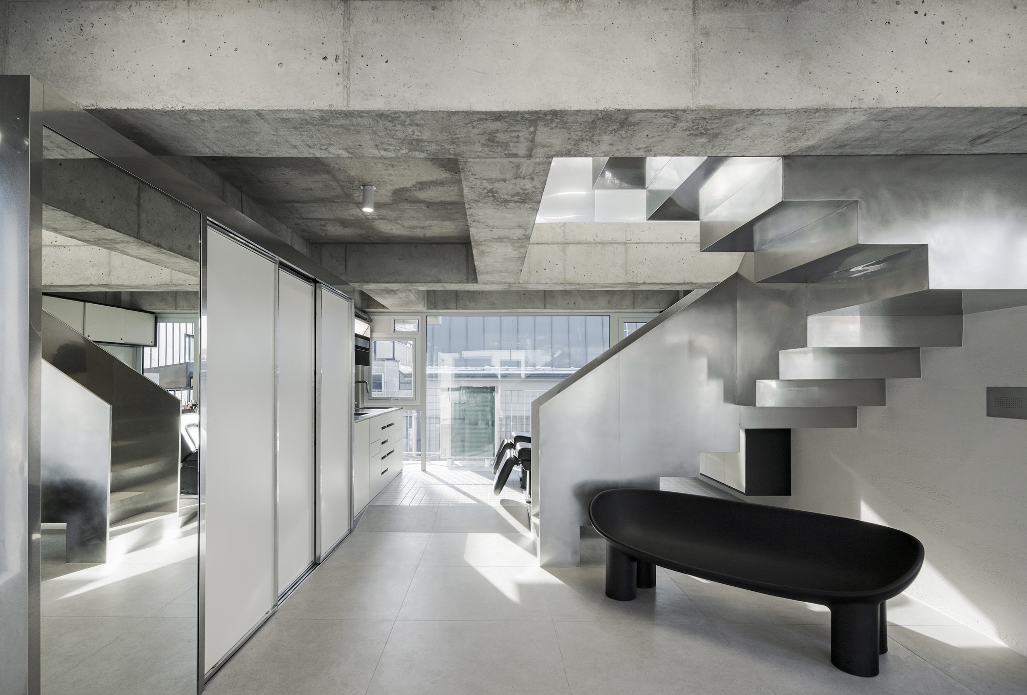 Interior view of the folded steel staircase rising against white walls beneath exposed concrete beams
