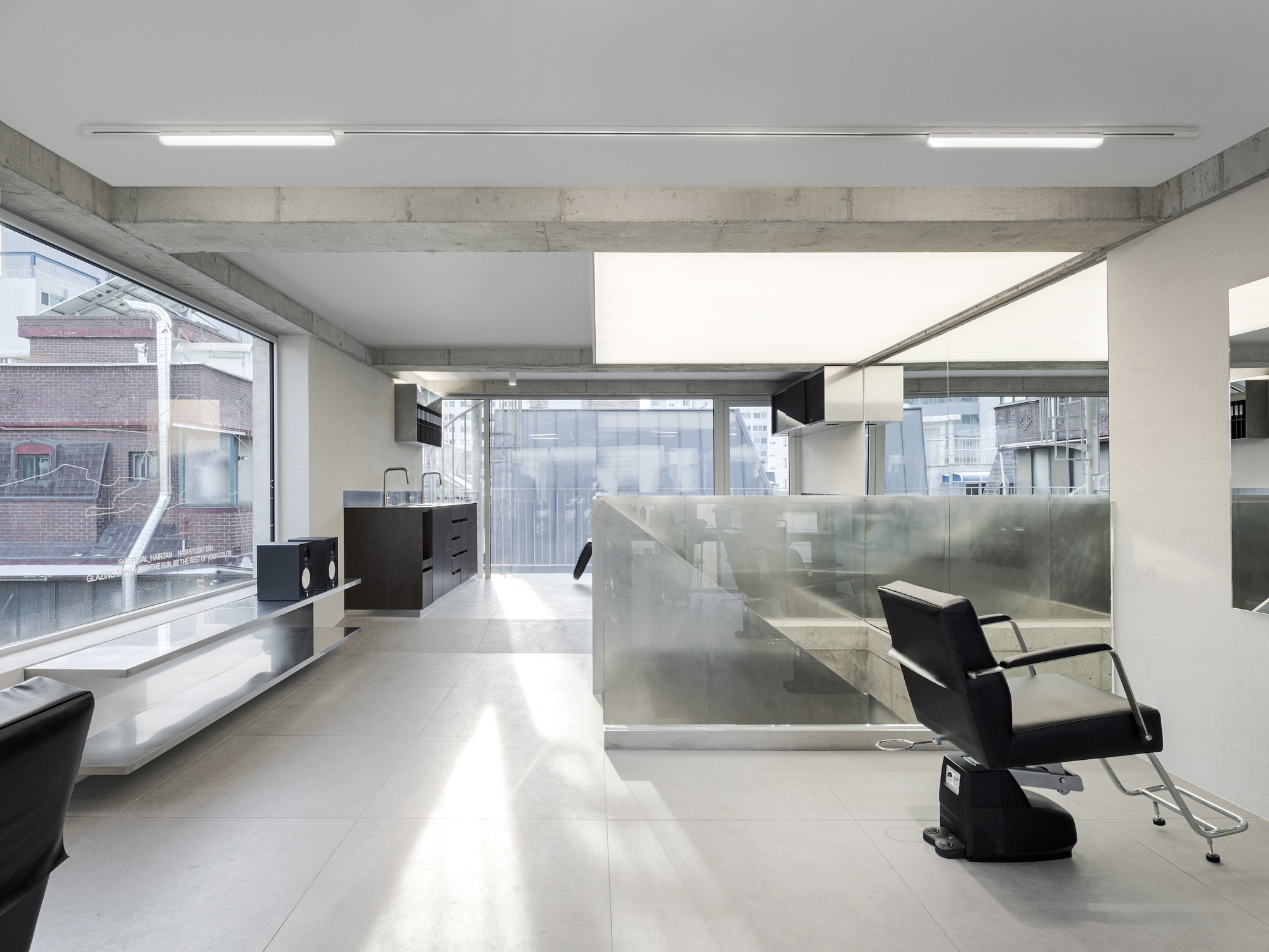 Open salon space with stainless steel partition walls and large windows overlooking neighboring buildings