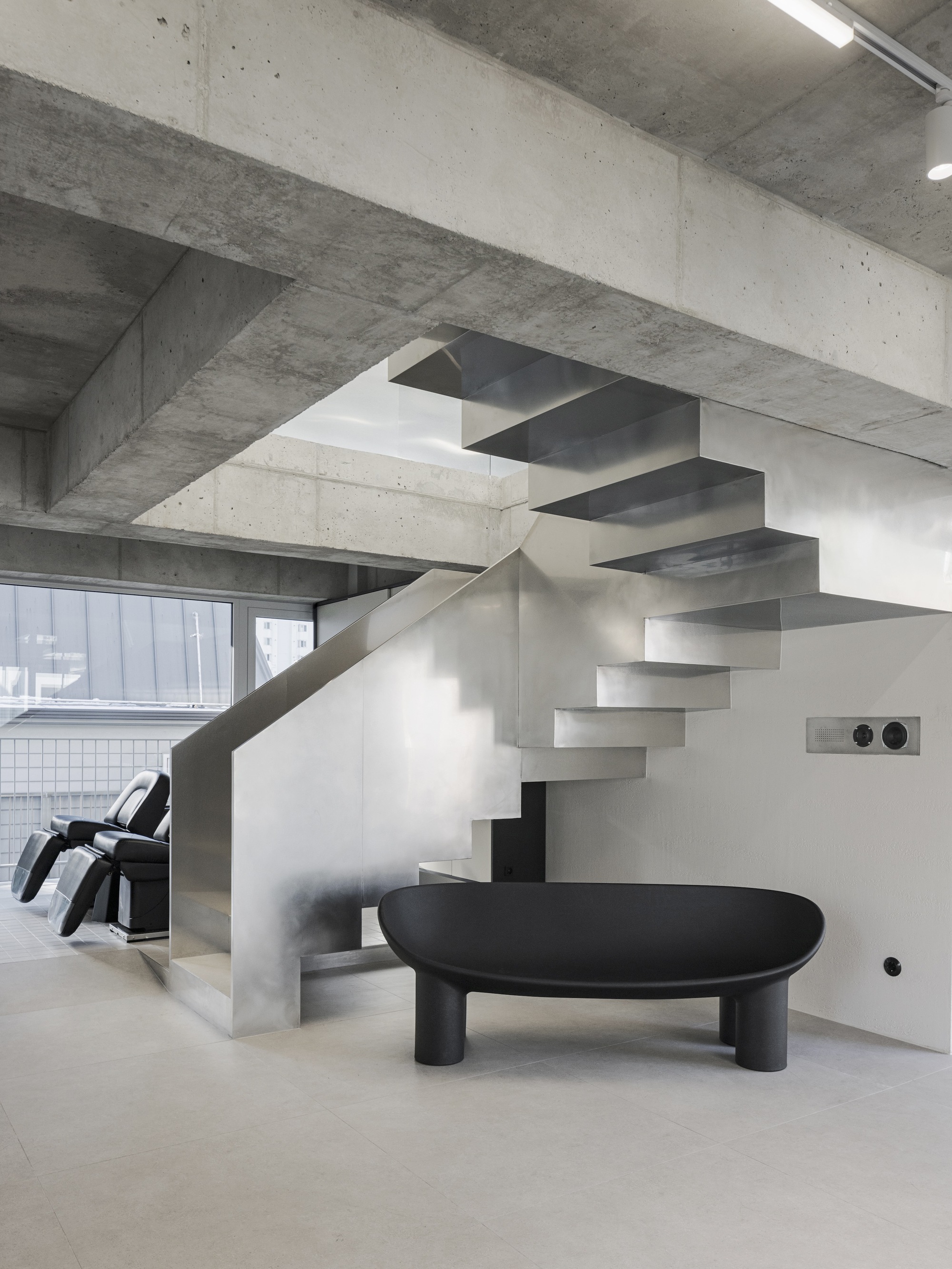 Close-up of the cantilevered steel staircase beside a low black table under concrete structure