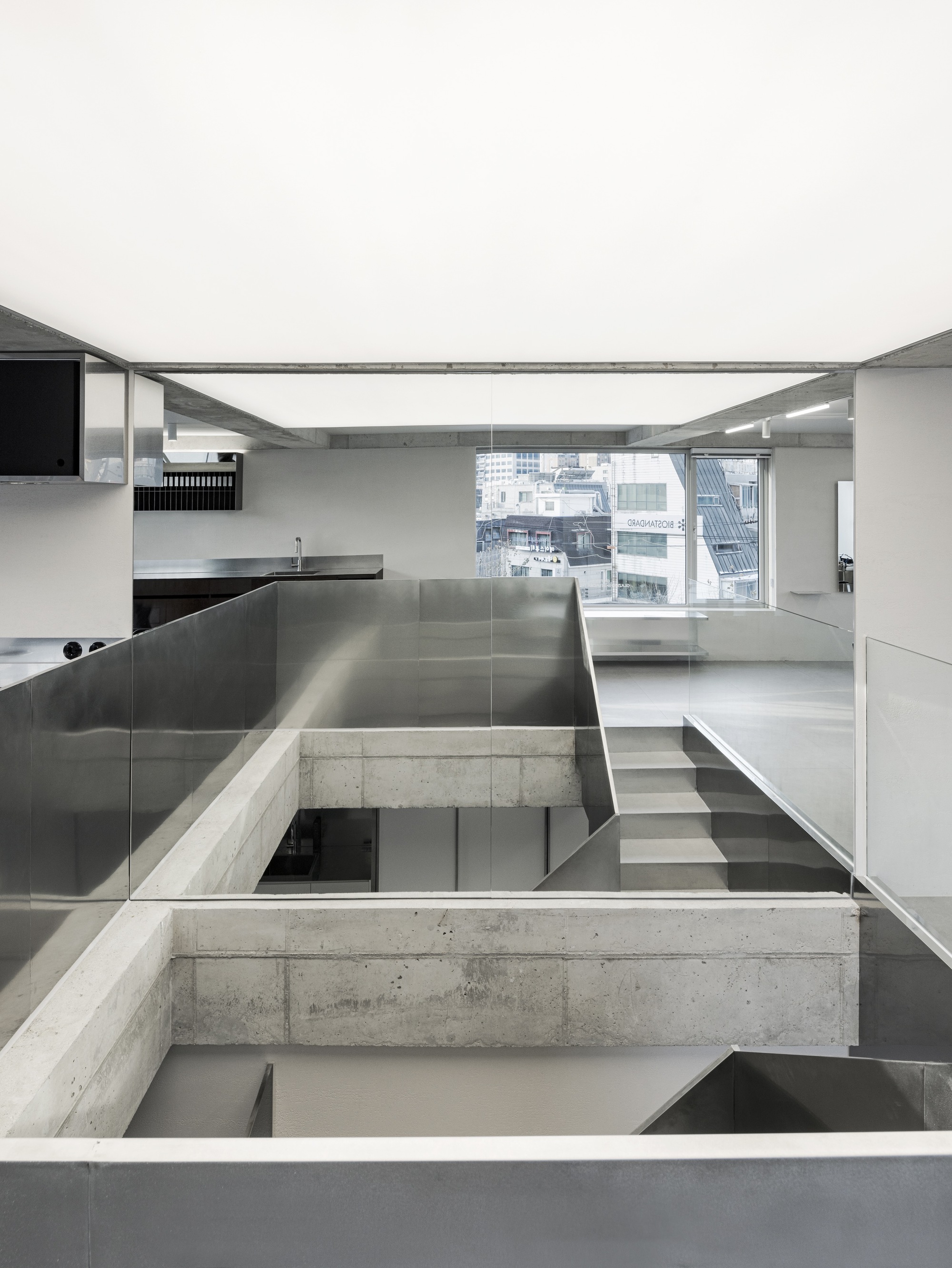 Split-level interior with stainless steel kitchen island and concrete beams crossing over glazed openings