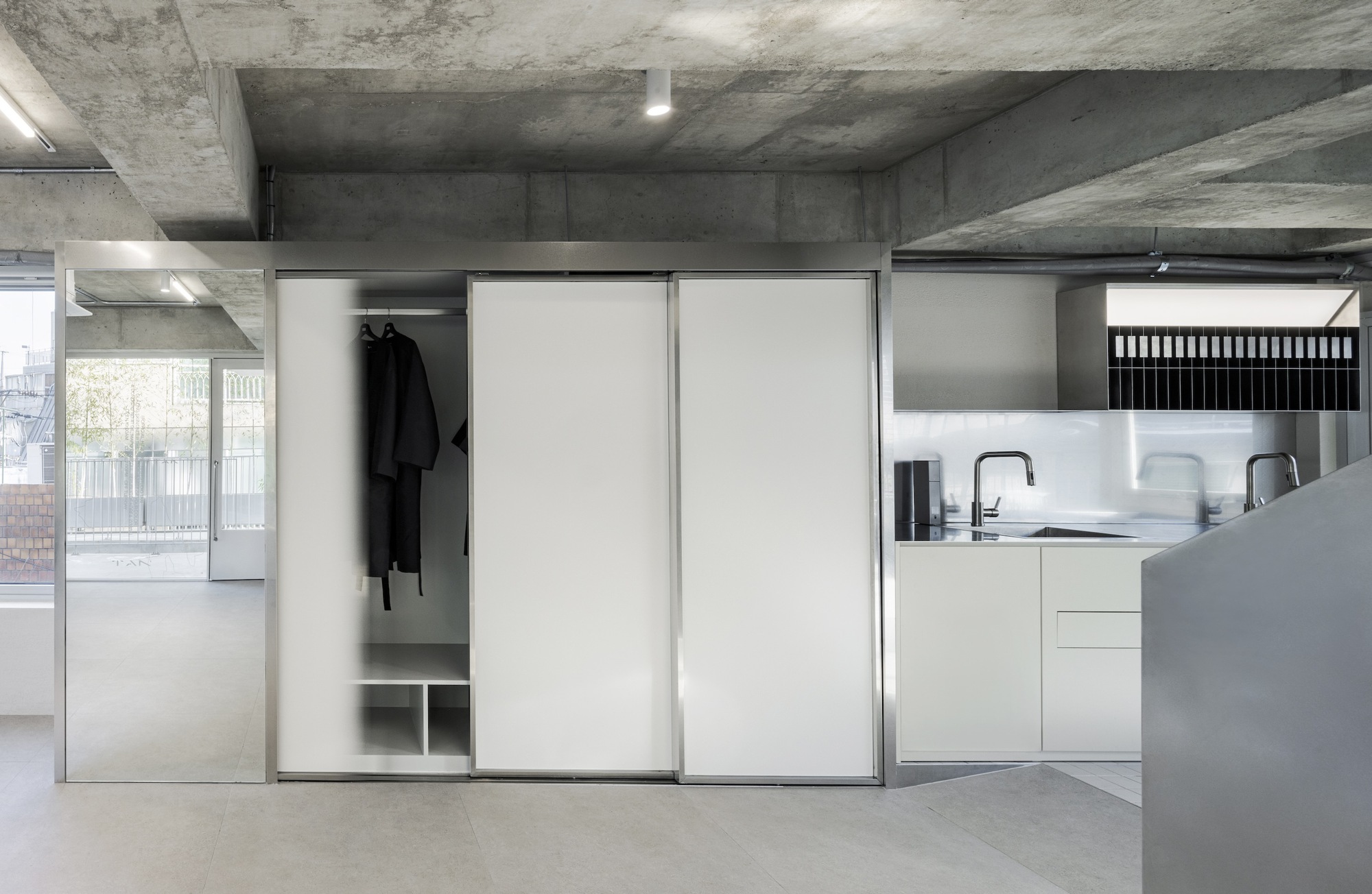 Sliding white wardrobe doors partially open to reveal hanging garments, beside a kitchen with white countertops