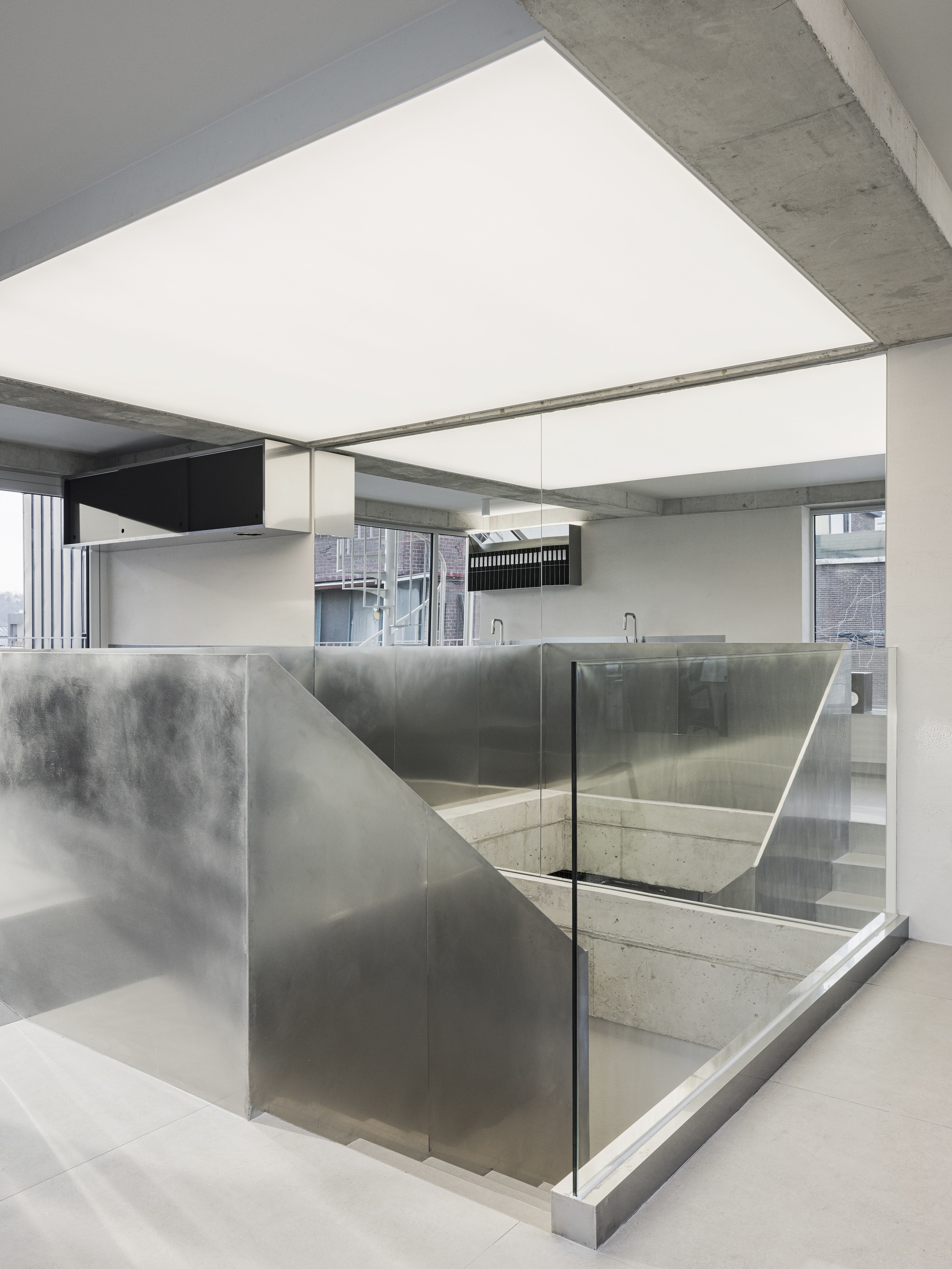 Concrete stairwell enclosed by translucent glass panels and brushed steel walls beneath an exposed ceiling