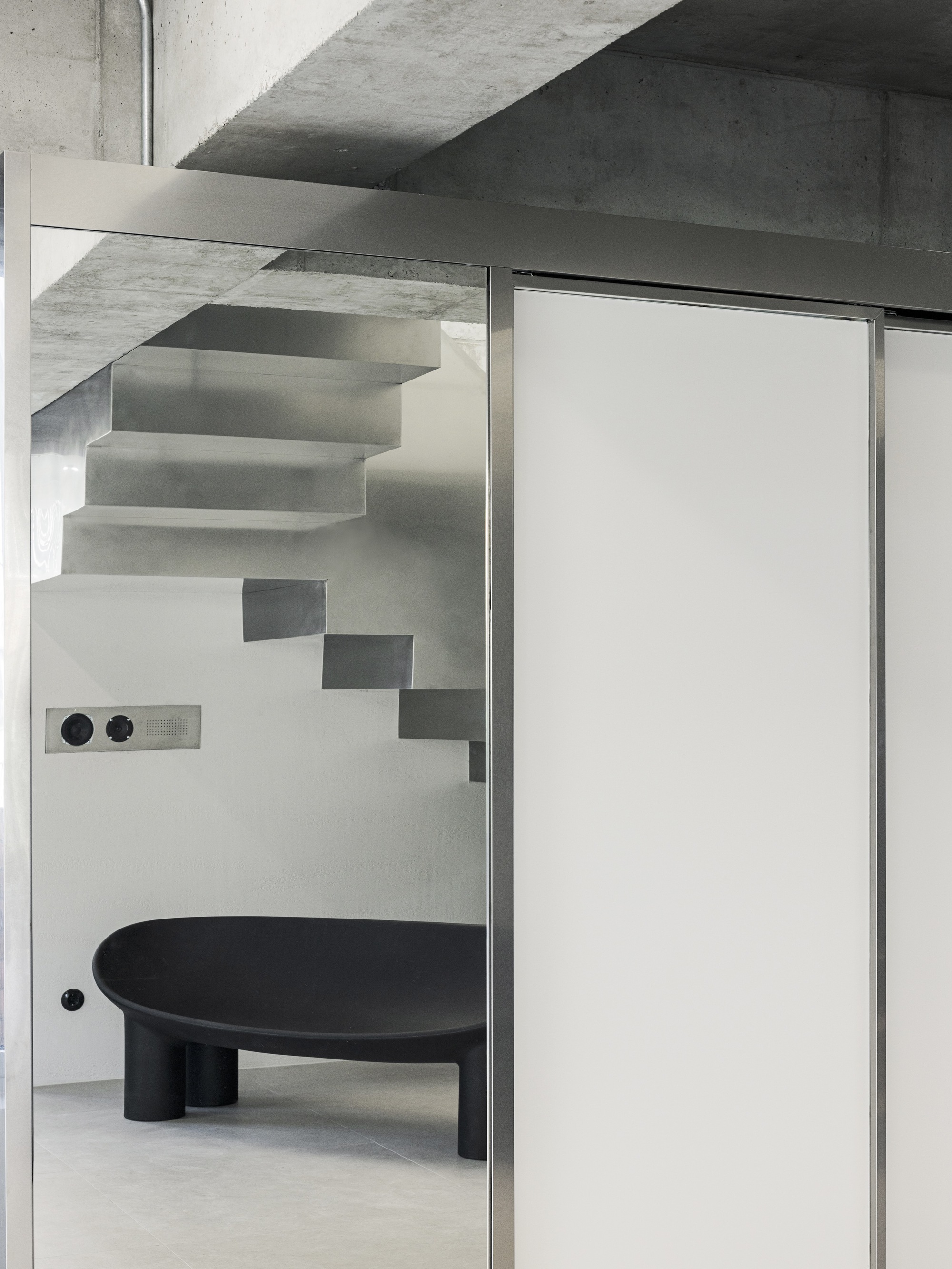 View through glass partition showing floating steel stairs and a black circular table below
