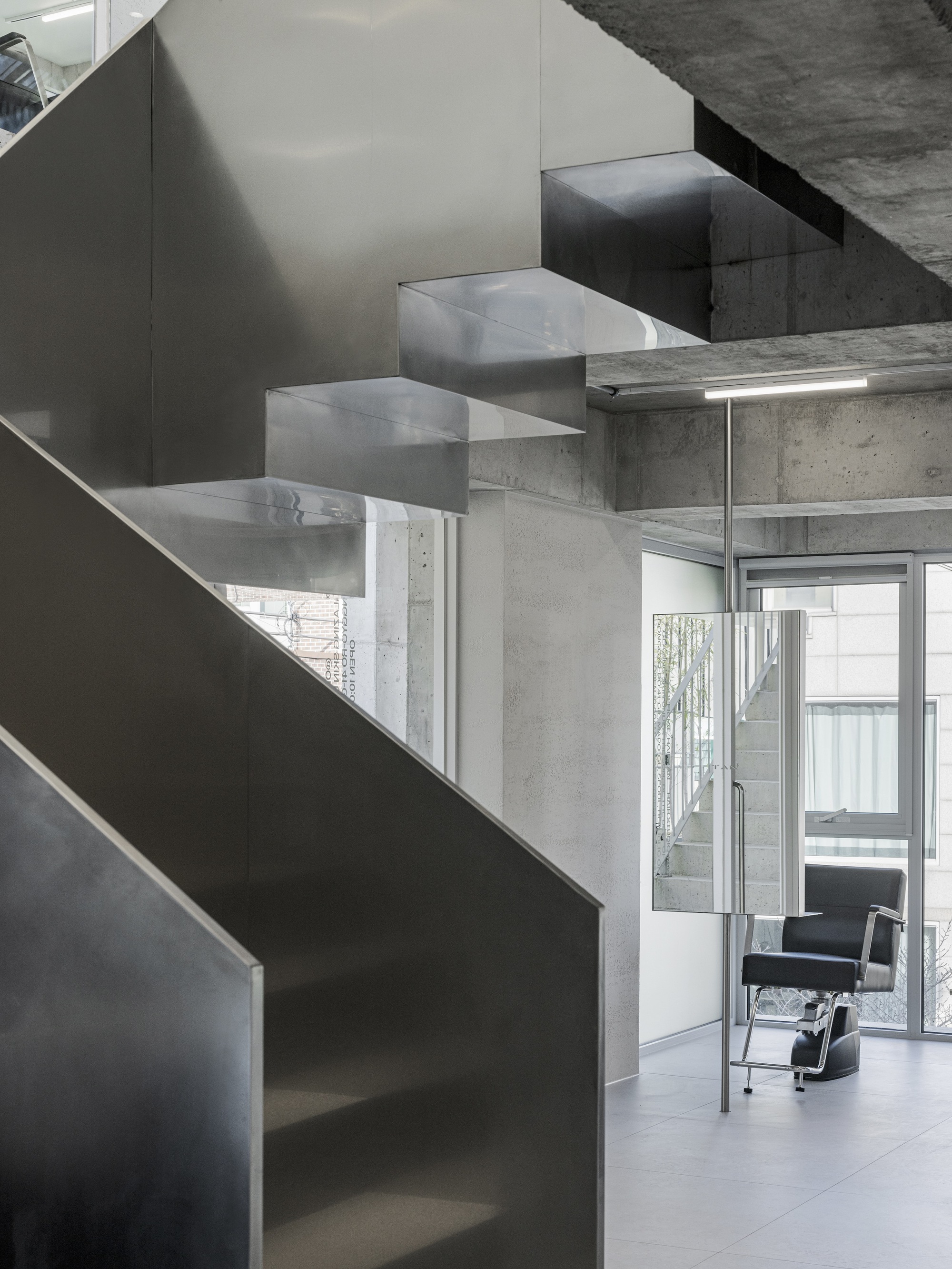 Steel staircase descending beside exposed concrete columns with a chair visible through the doorway