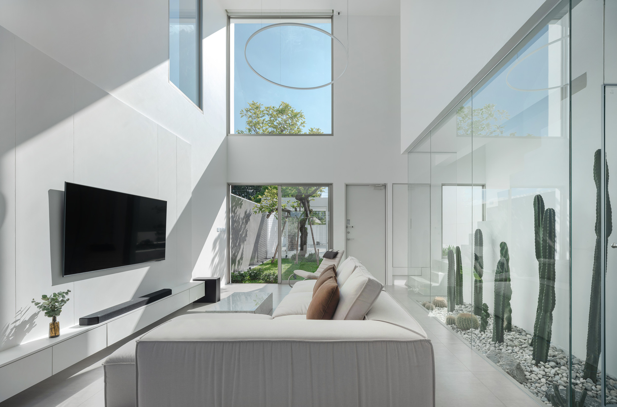 Double-height living room with glass courtyard separating cacti garden from interior seating under afternoon sunlight