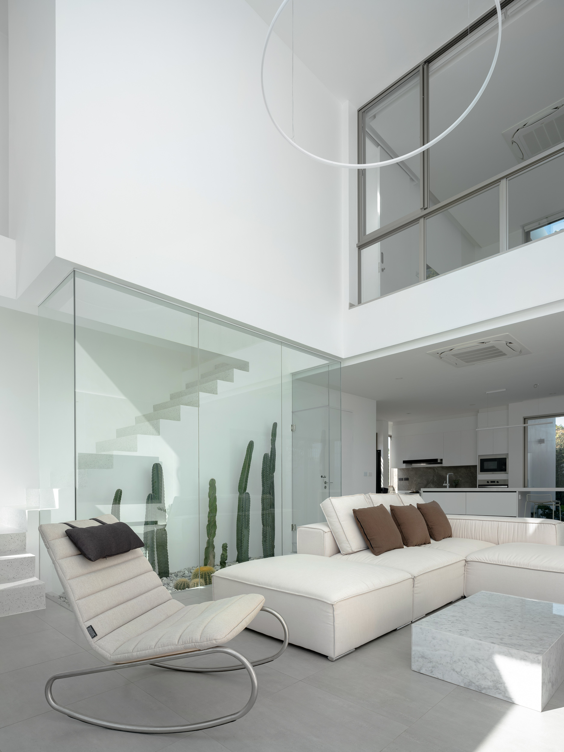 Living space with glass-enclosed staircase, suspended ring light, and tall cacti visible through glass partition