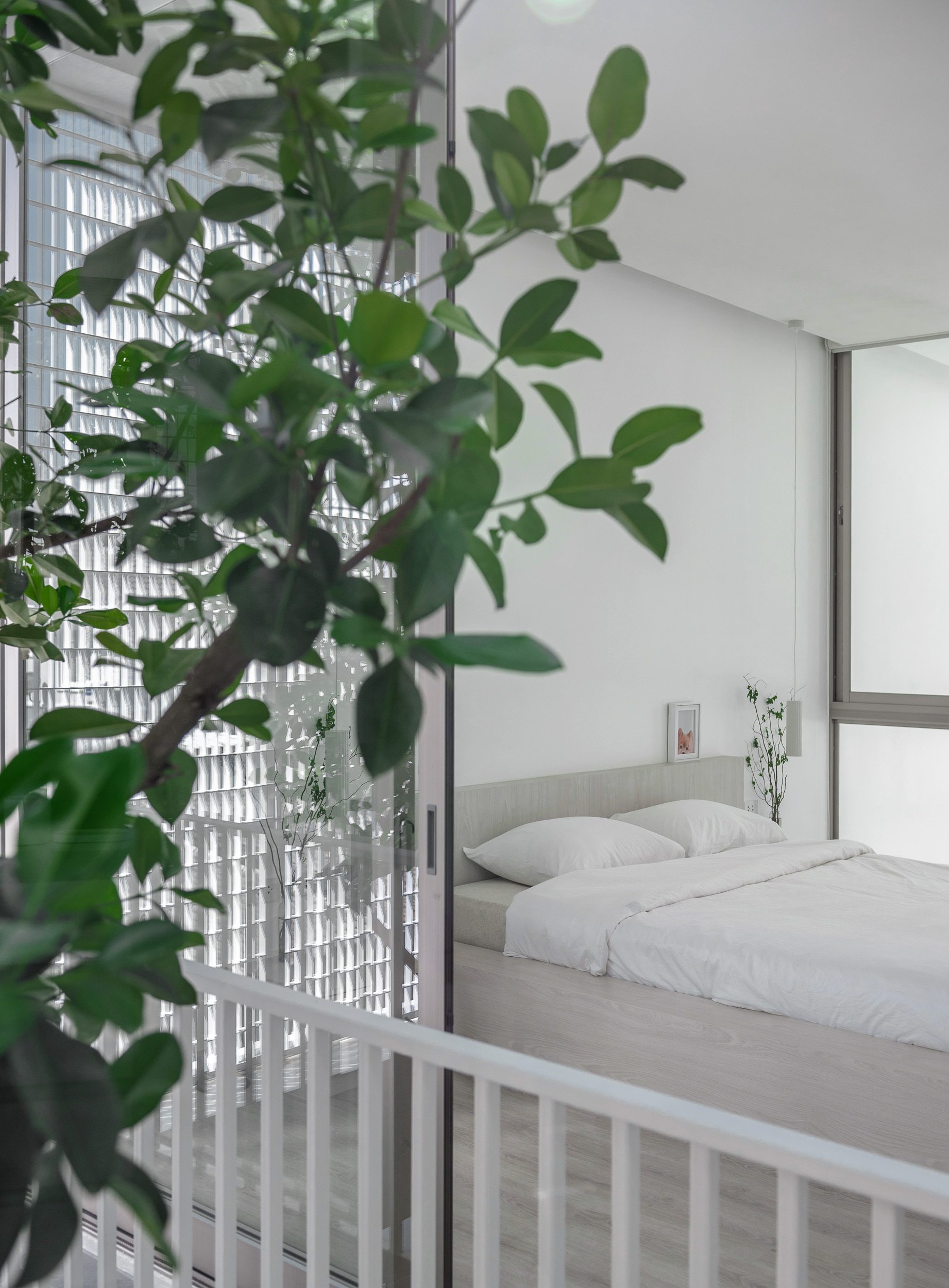 Sleeping platform viewed through white railings with foliage and glass block wall in the foreground
