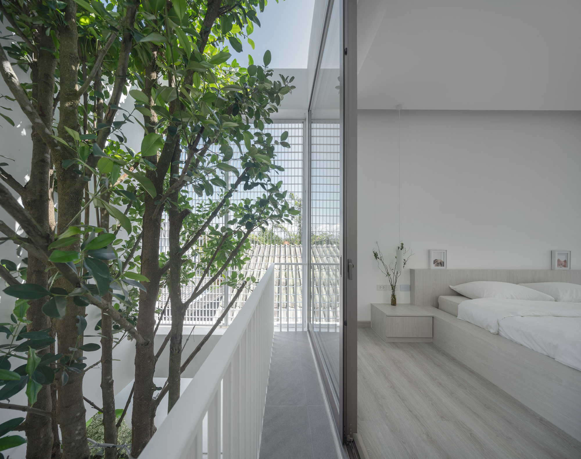 Bedroom opening to a narrow balcony with white vertical railings and trees behind glass block screens