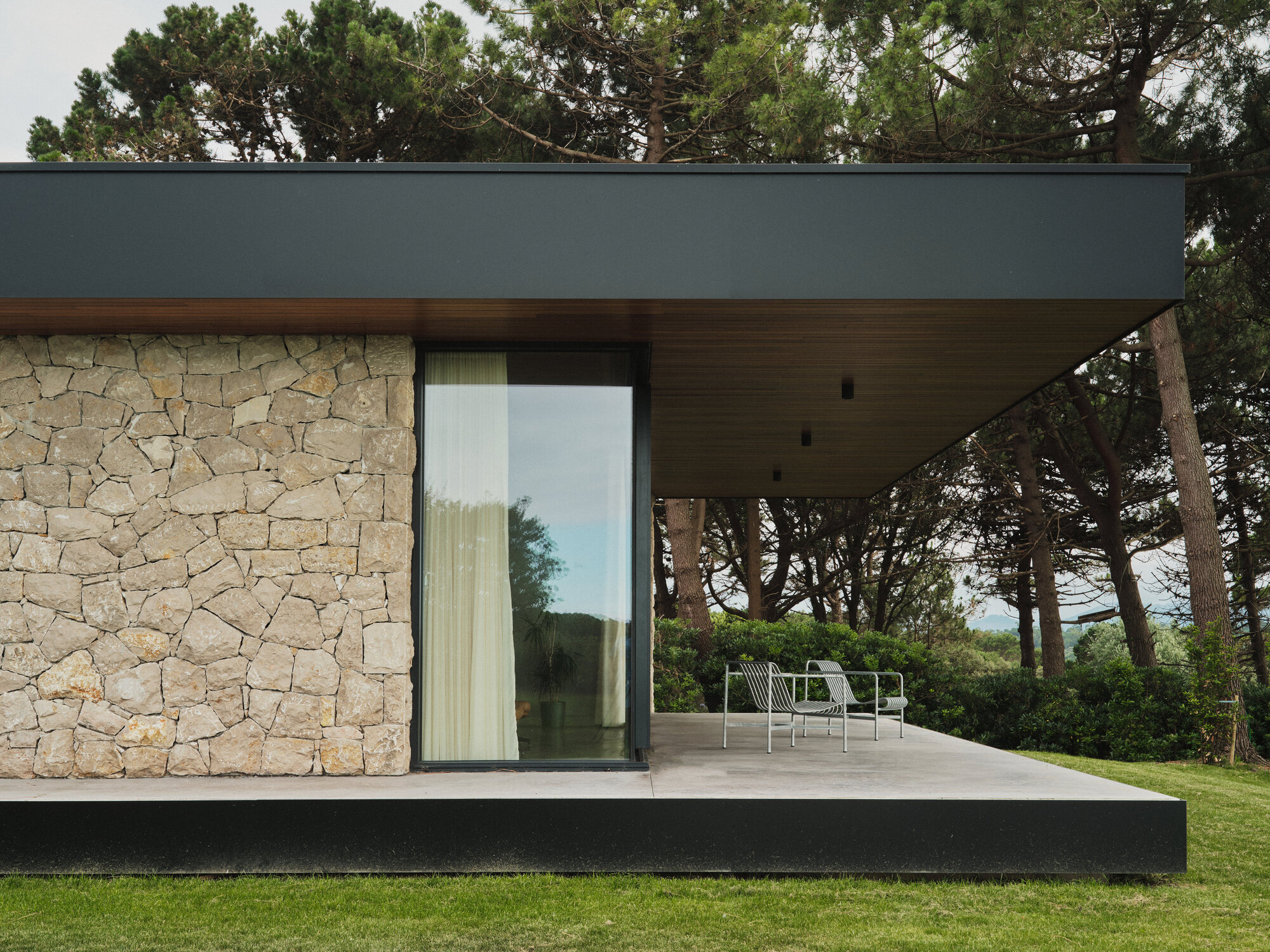 Facade detail with stone wall, sliding glass door and recessed timber soffit above concrete terrace