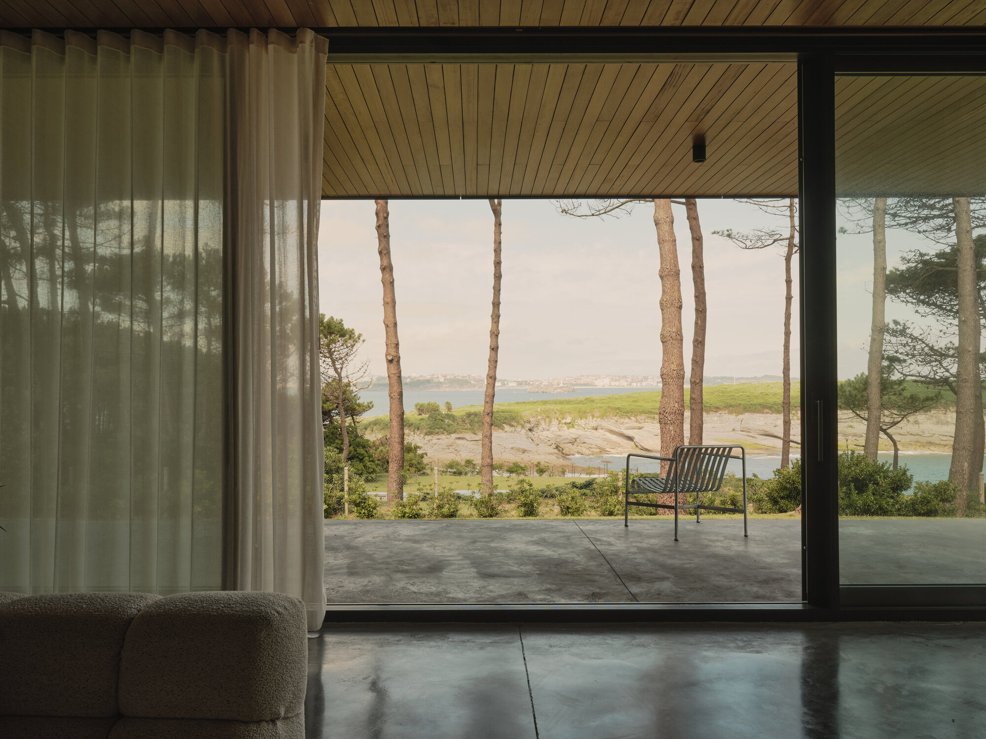 Floor-to-ceiling glazing framing a covered terrace with views of water and pine trees