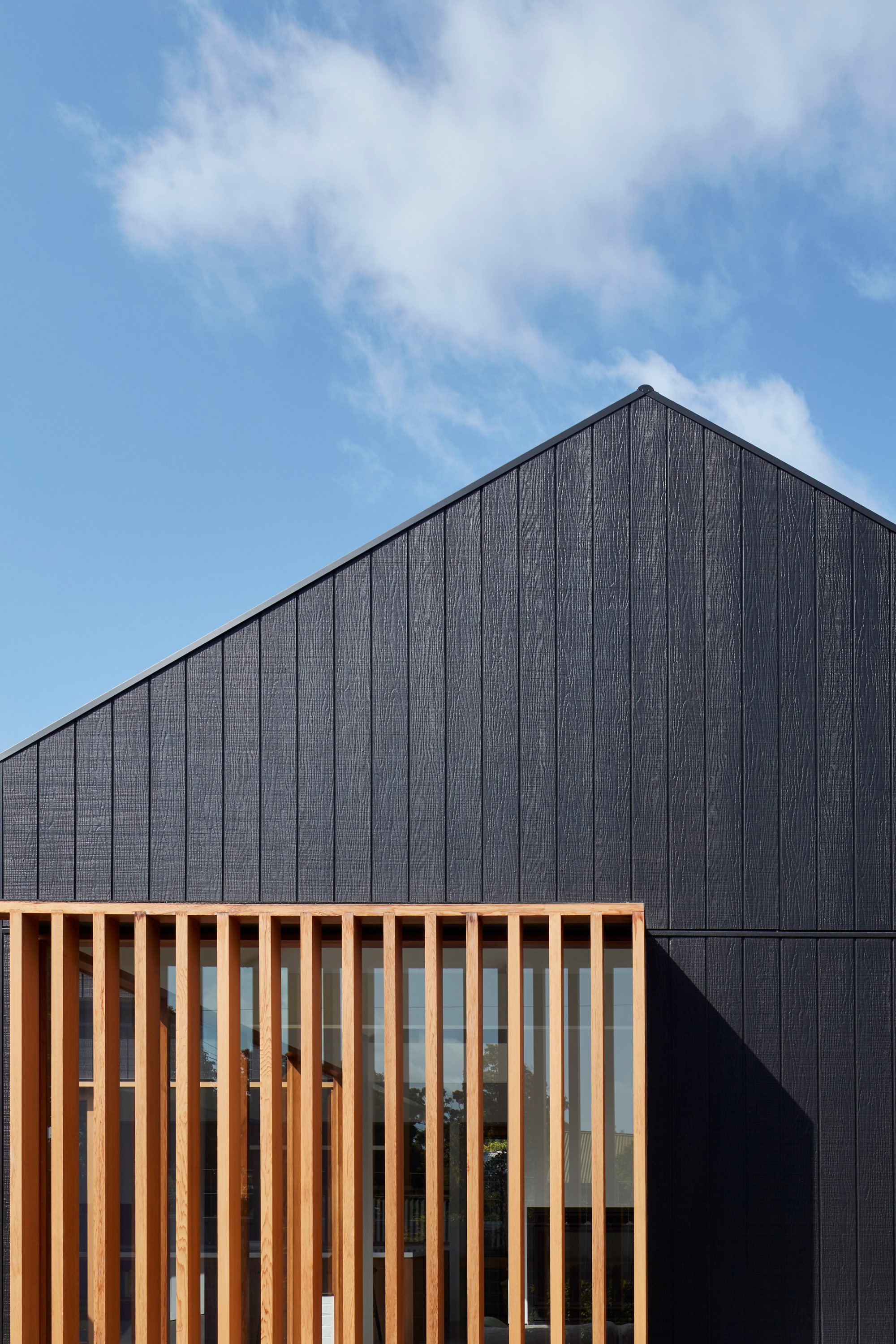 Close-up of the vertical timber screen against the black cladding beneath wispy clouds