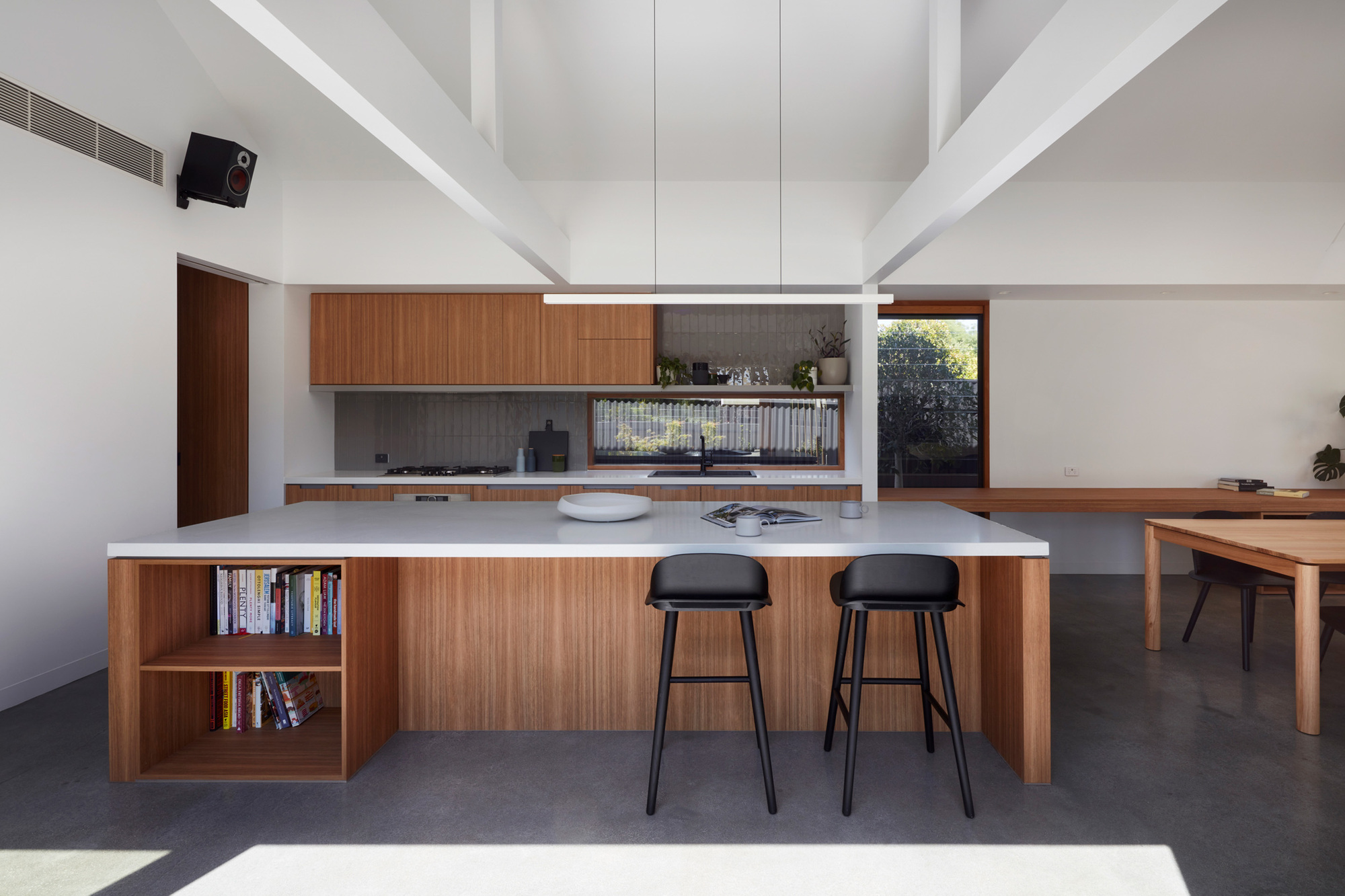Kitchen island with timber cabinetry and white stone countertop beneath exposed white beams and clerestory skylights